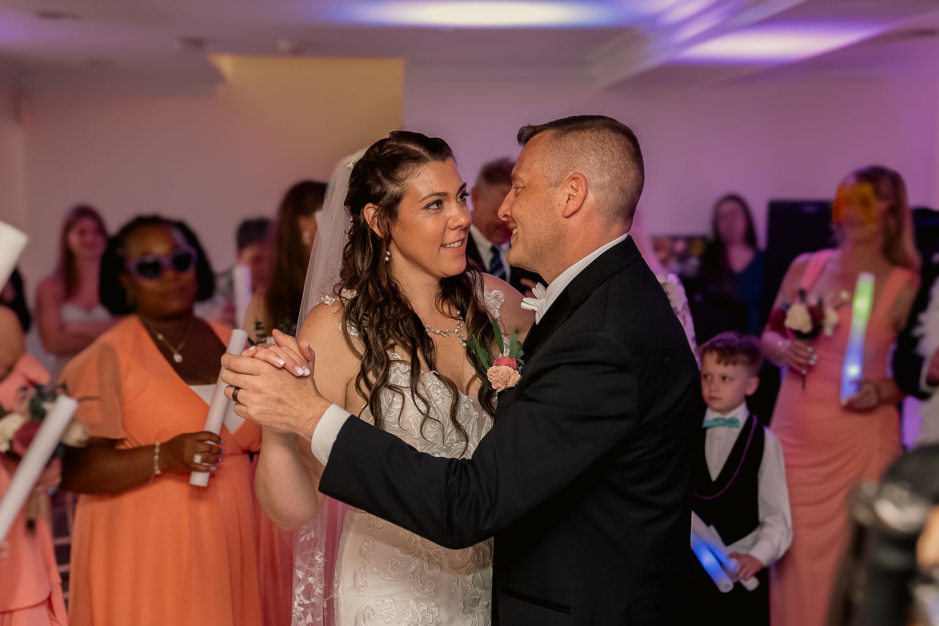 A bride and groom share a dance at a wedding reception, surrounded by guests holding light-up glow sticks.