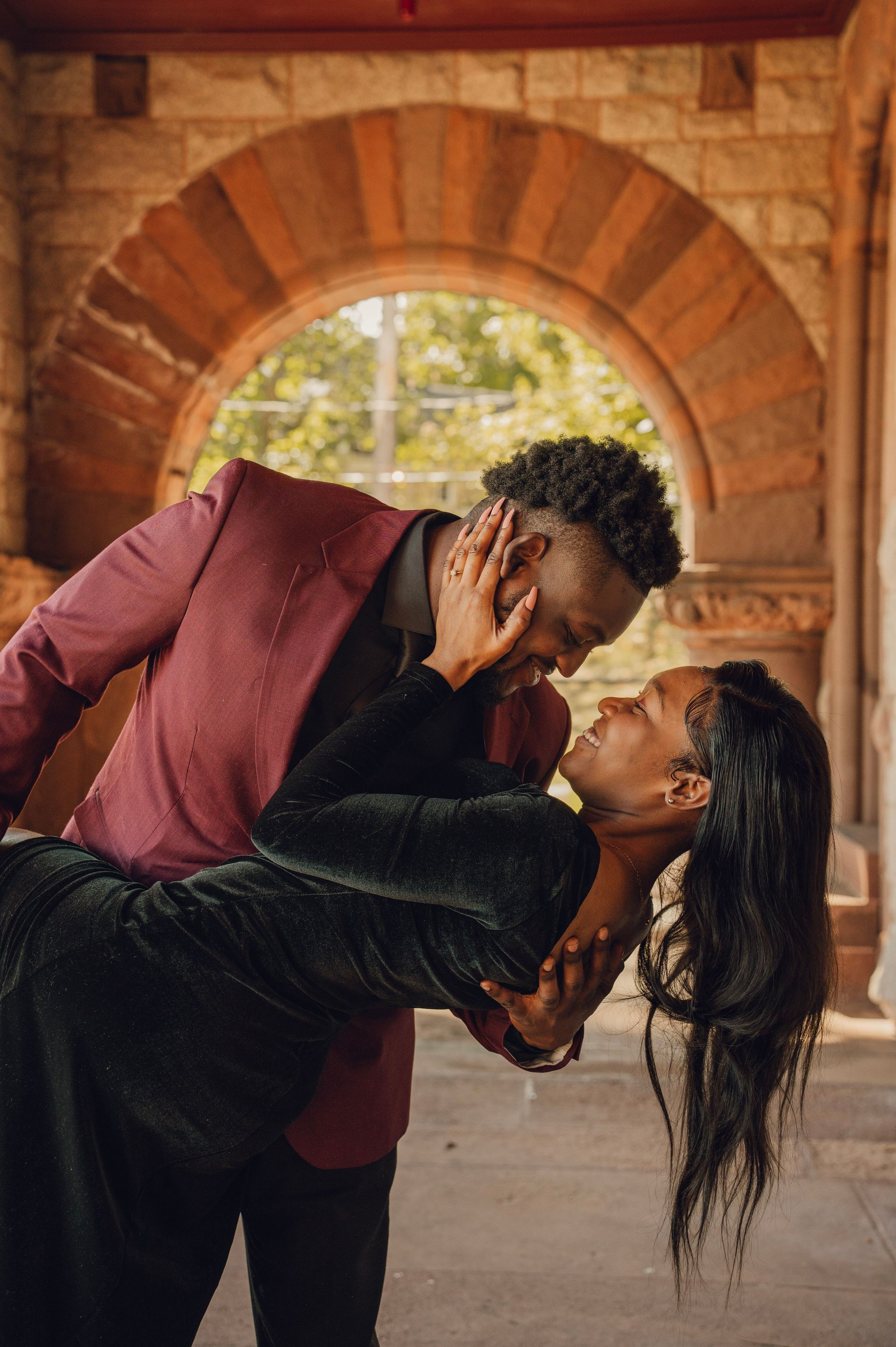 A couple in formal attire embracing and dancing under a stone archway in a warm, dimly lit setting.