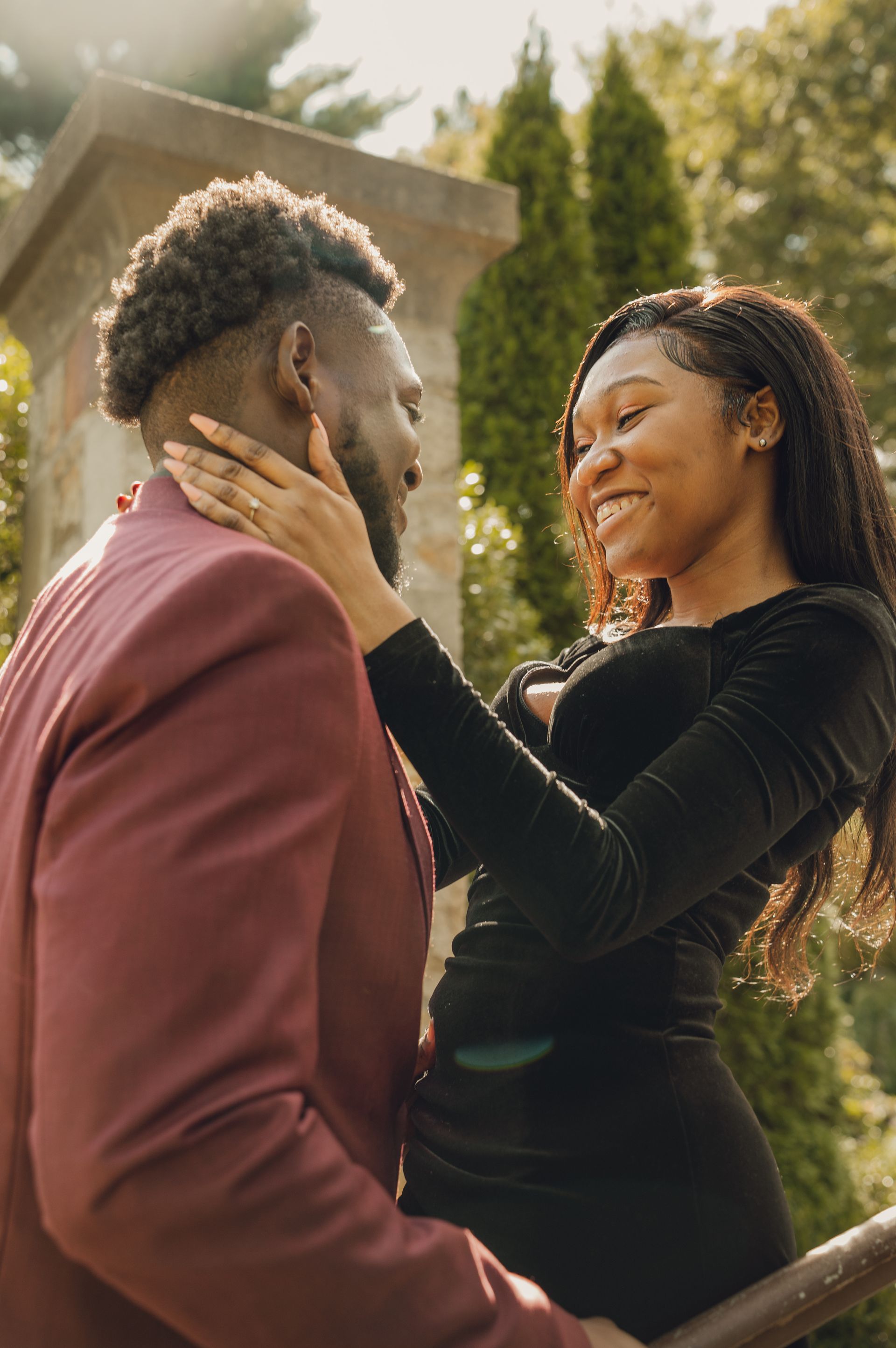 A couple embraces affectionately outdoors, with one person holding the other's face as they gaze at each other.