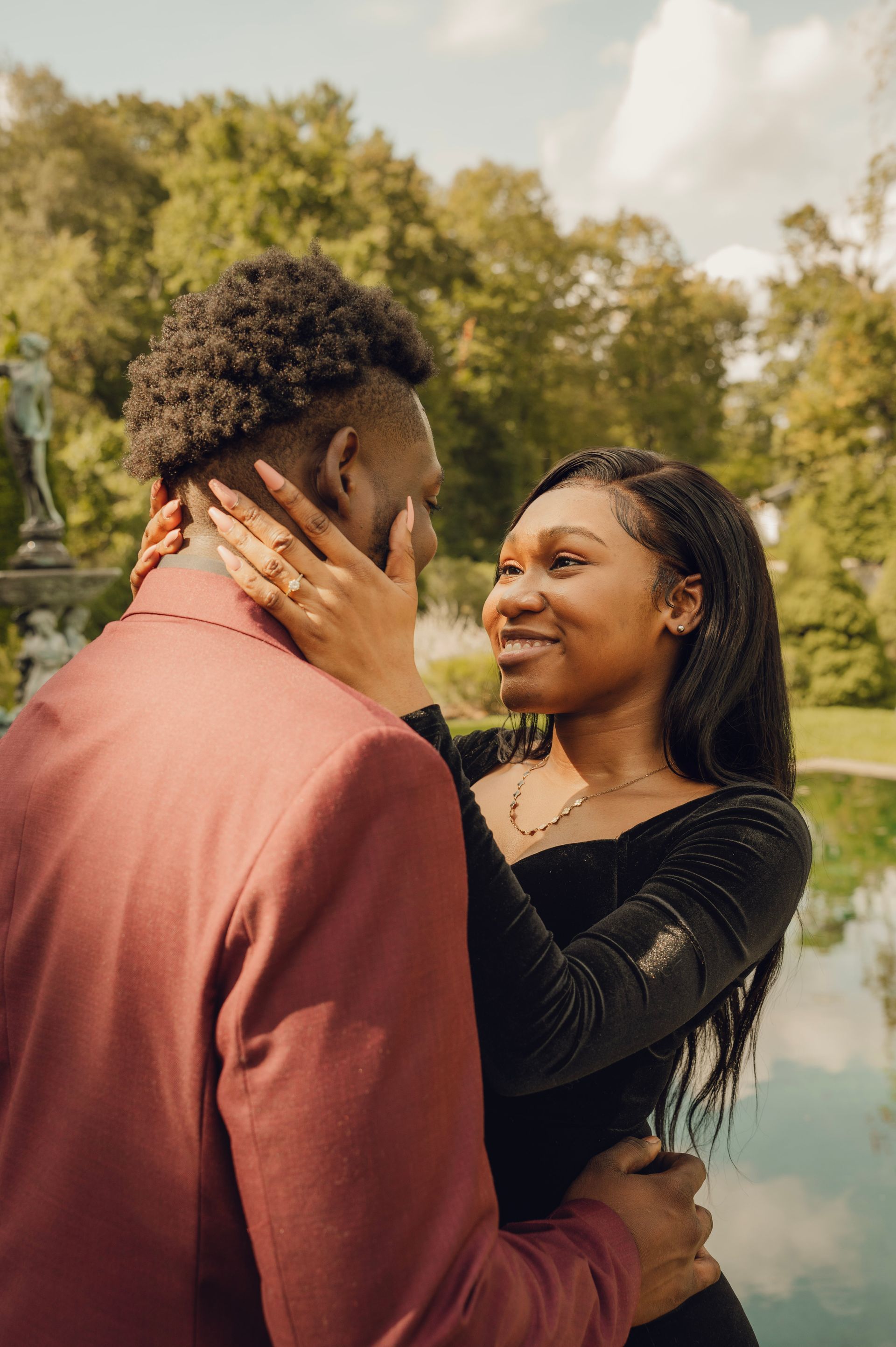 Two people in formal attire look at each other lovingly in a garden, with one person holding the other's face.