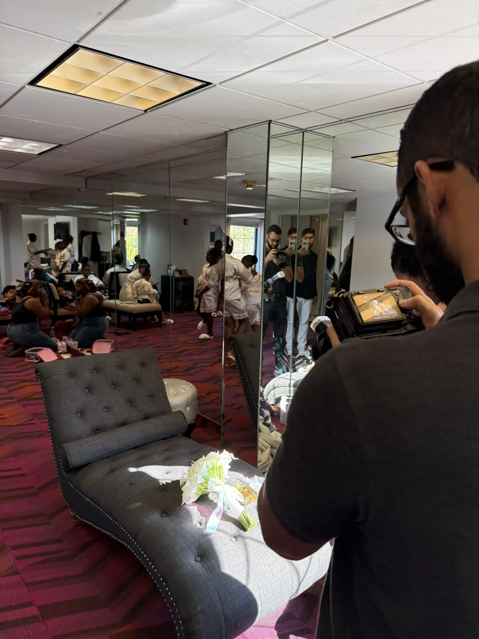 A photographer in a room with mirrored walls captures a scene of people relaxing on lounge furniture.