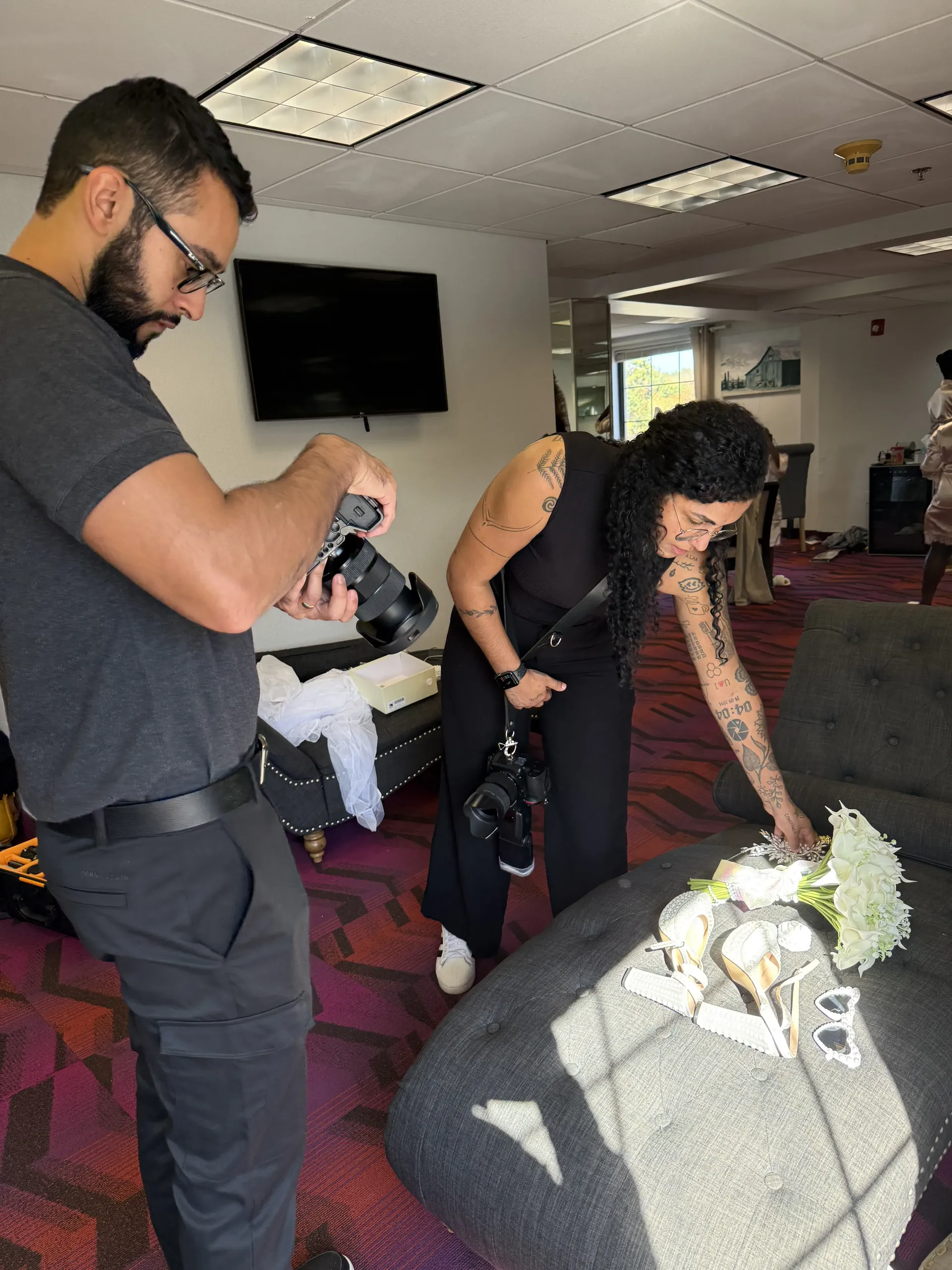 Two photographers work together to capture a close-up shot of a bridal bouquet resting on a dark gray couch.