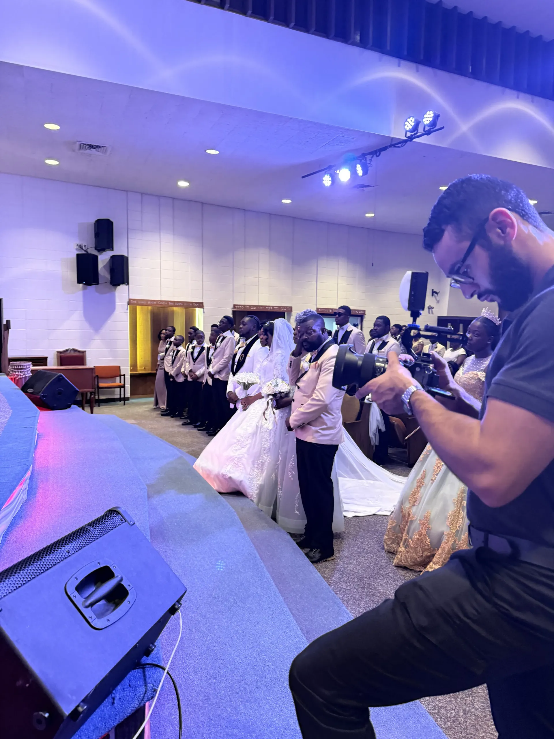 A videographer captures a wedding ceremony in a church with a bridal party standing at the altar.