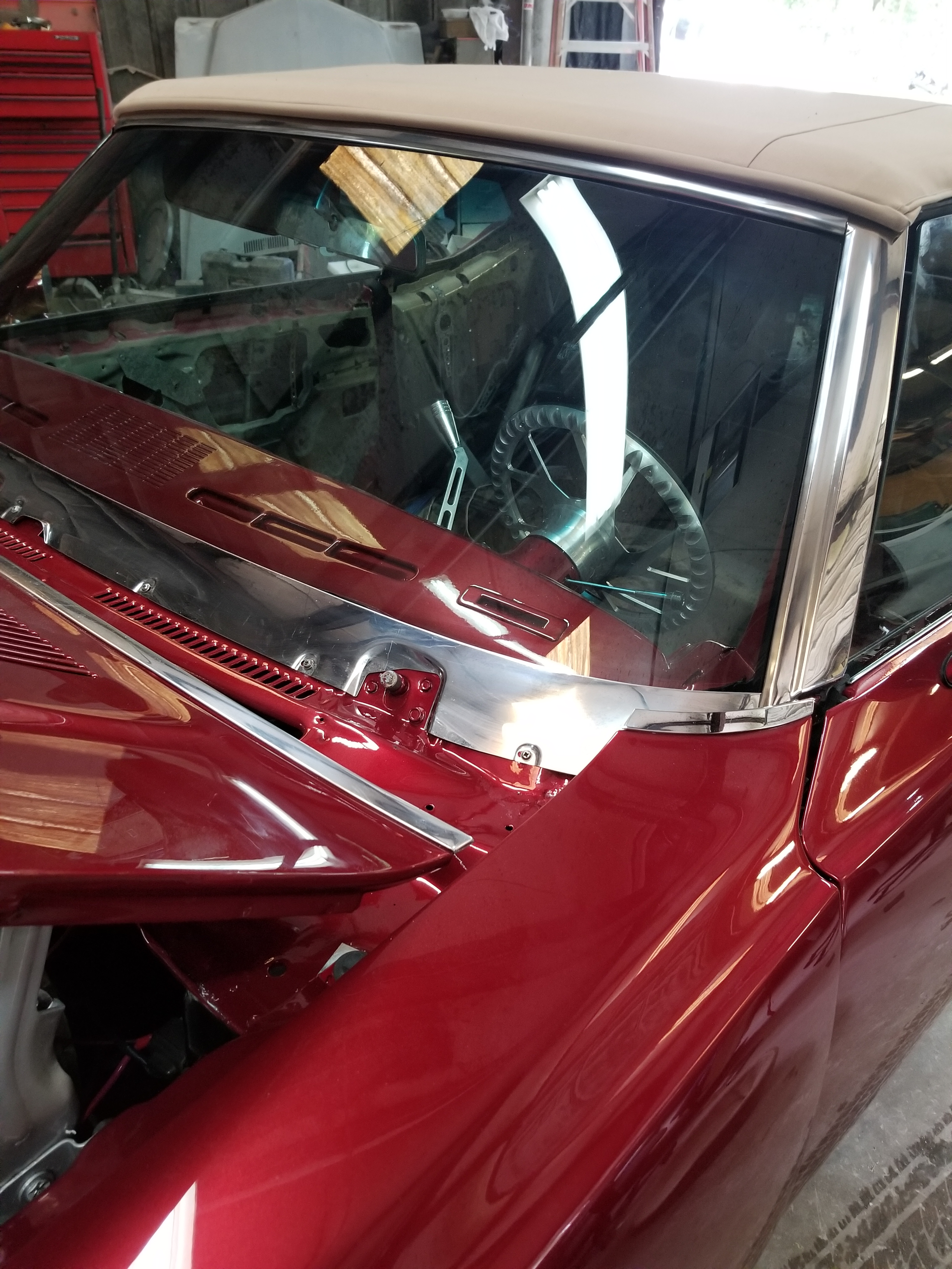 Mechanic installing a car windshield, using suction cups and a tool, in a garage.