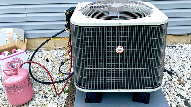 Air conditioning unit being serviced outdoors, with a pink refrigerant tank attached.