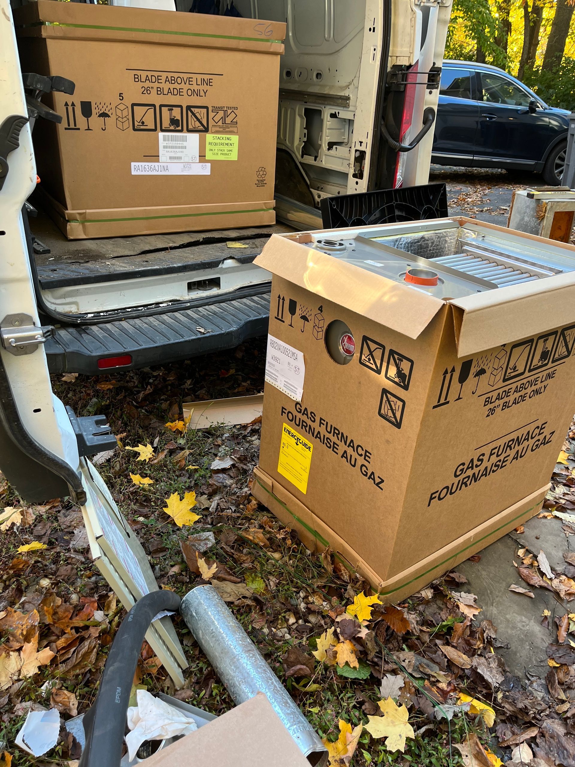 Boxes being unloaded from a van. One box open, others closed, outside on a leaf-covered surface.