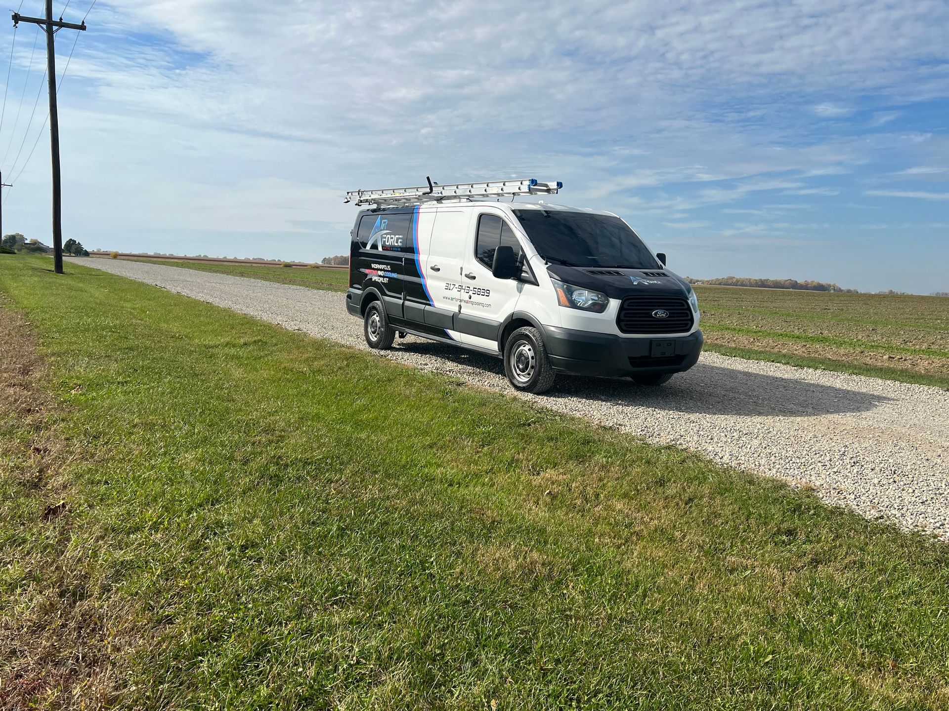 White service van on a gravel road, parked on a grassy area under a blue sky.