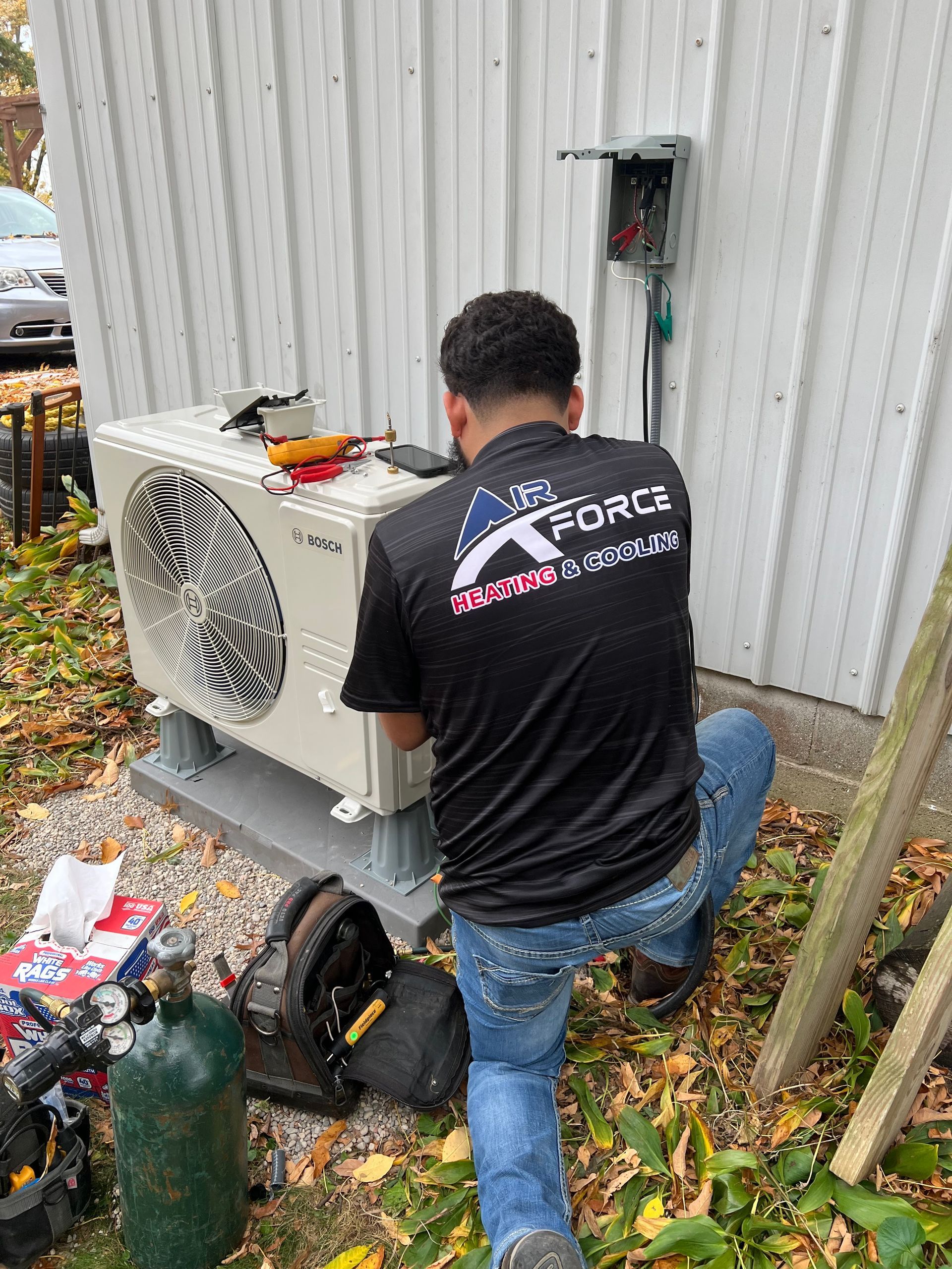 HVAC technician installs a heat pump unit outside a building, tools and equipment nearby.