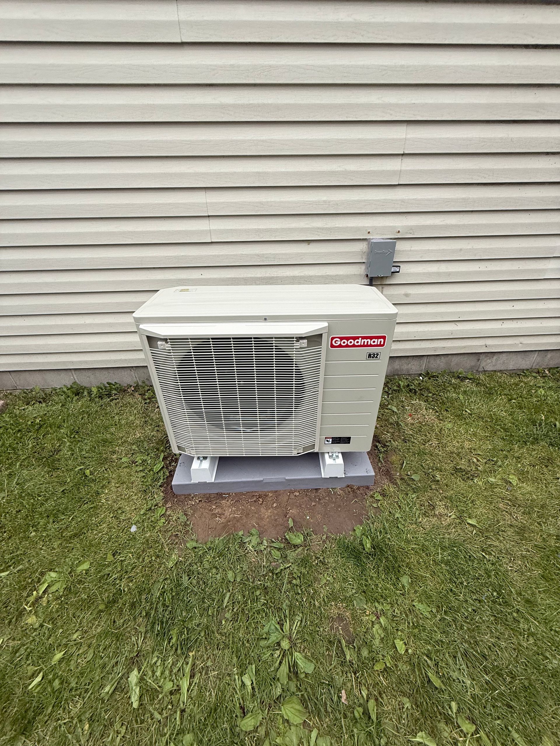Air conditioning unit outside a house, set on concrete blocks.