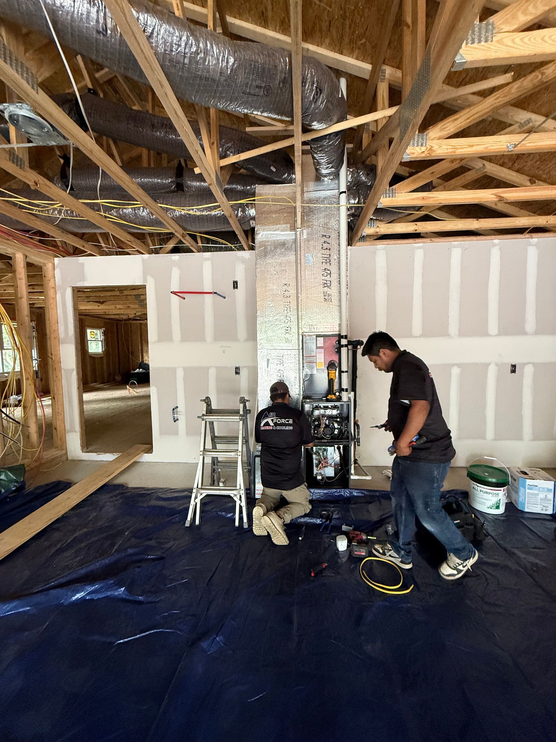 Two workers installing HVAC unit in a room under construction.