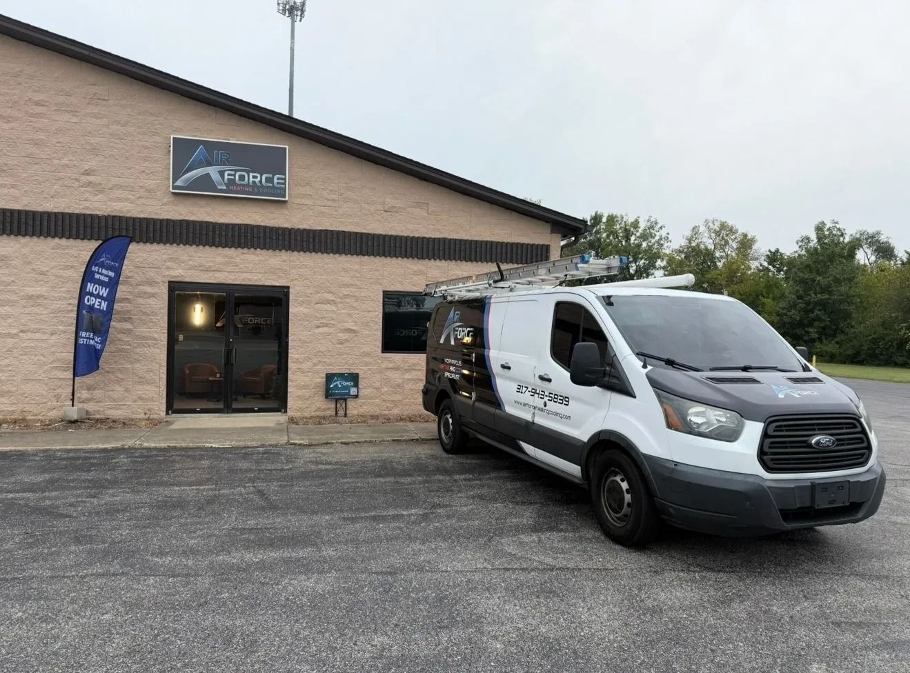 White cargo van parked outside a beige brick office building with a blue sign and blue flag banner.