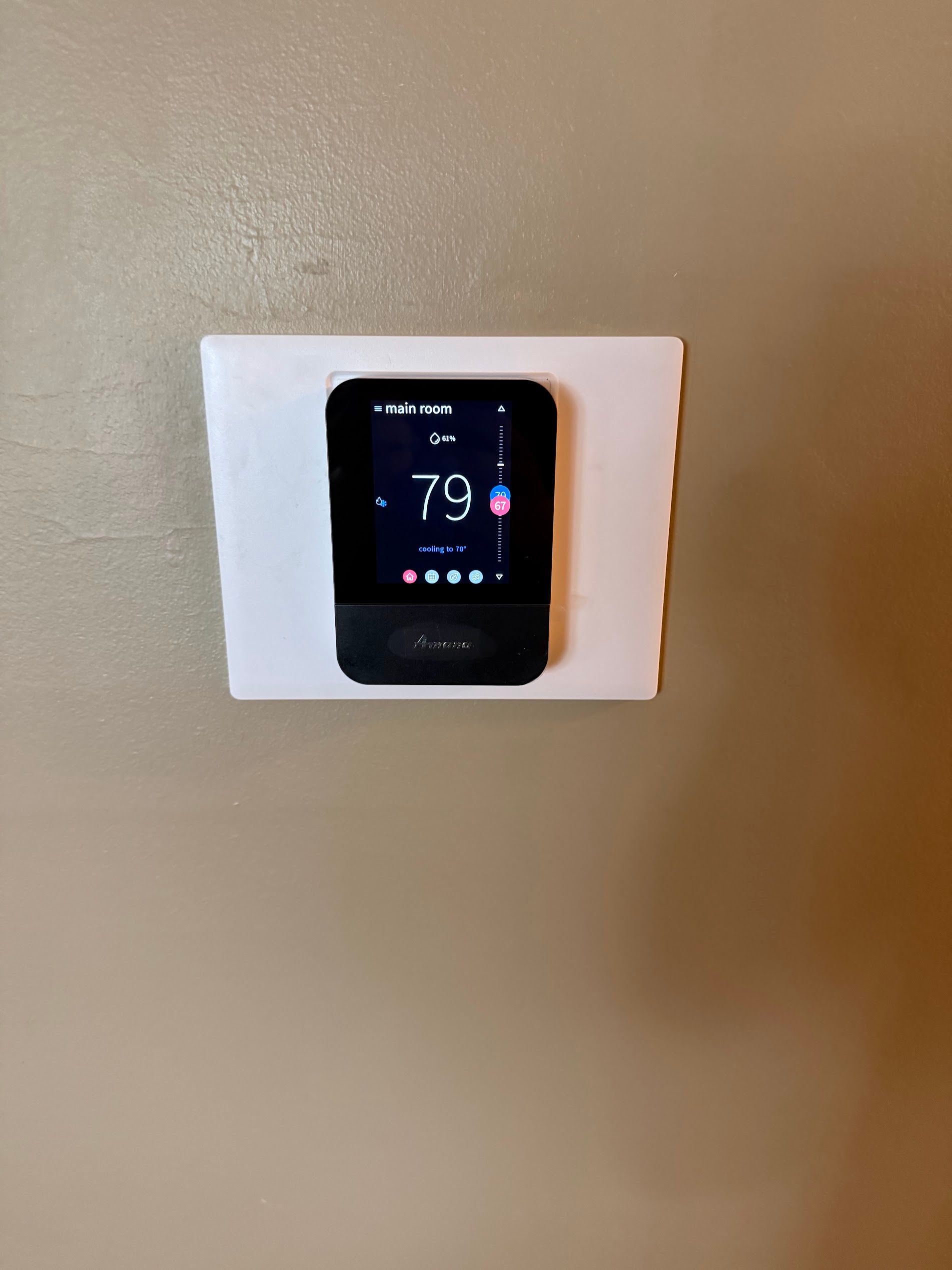 Wall-mounted thermostat on a beige wall displaying 79°F, framed by a white plate.