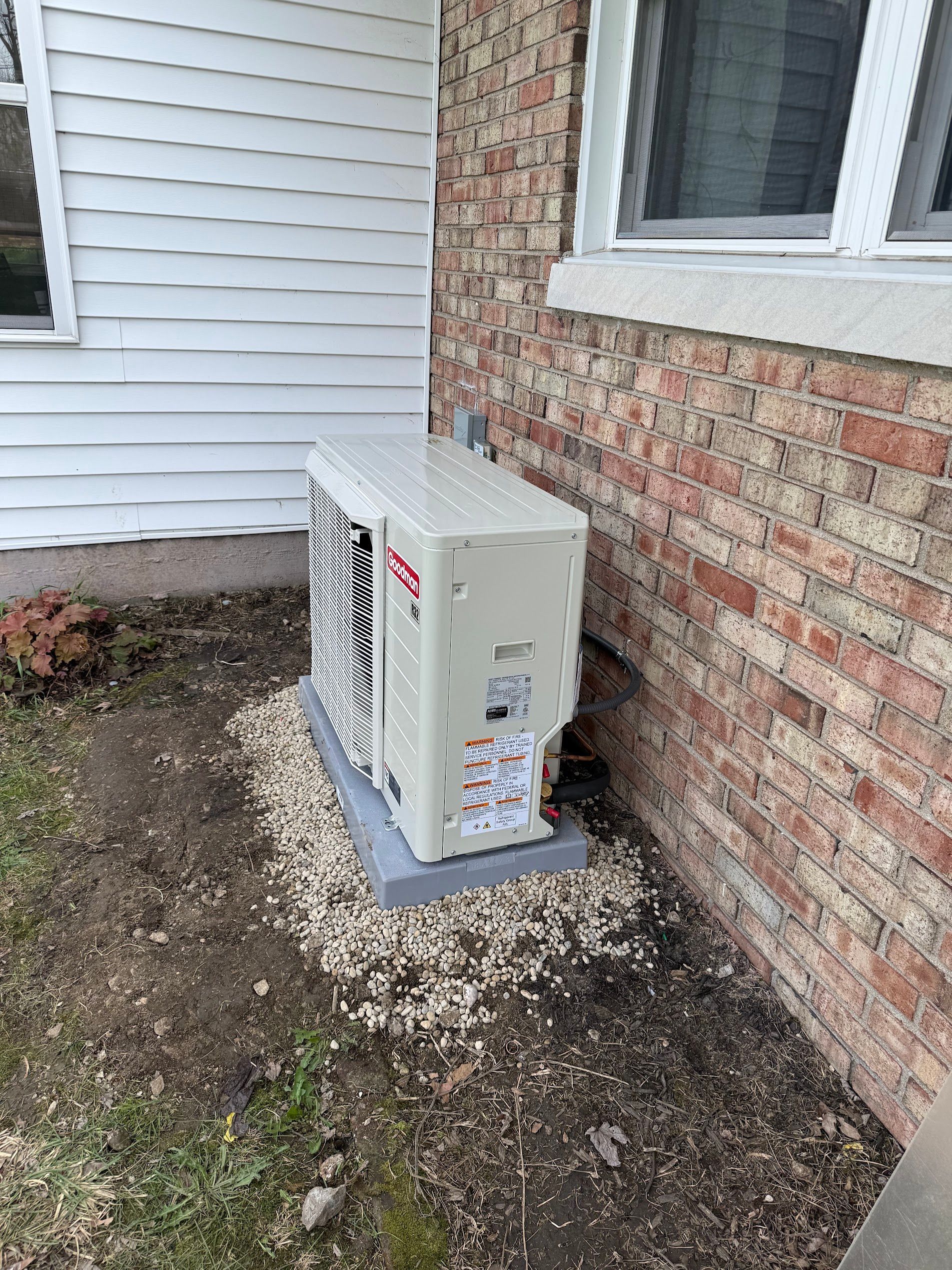 Outdoor HVAC unit beside a brick house and white siding on a gravel patch