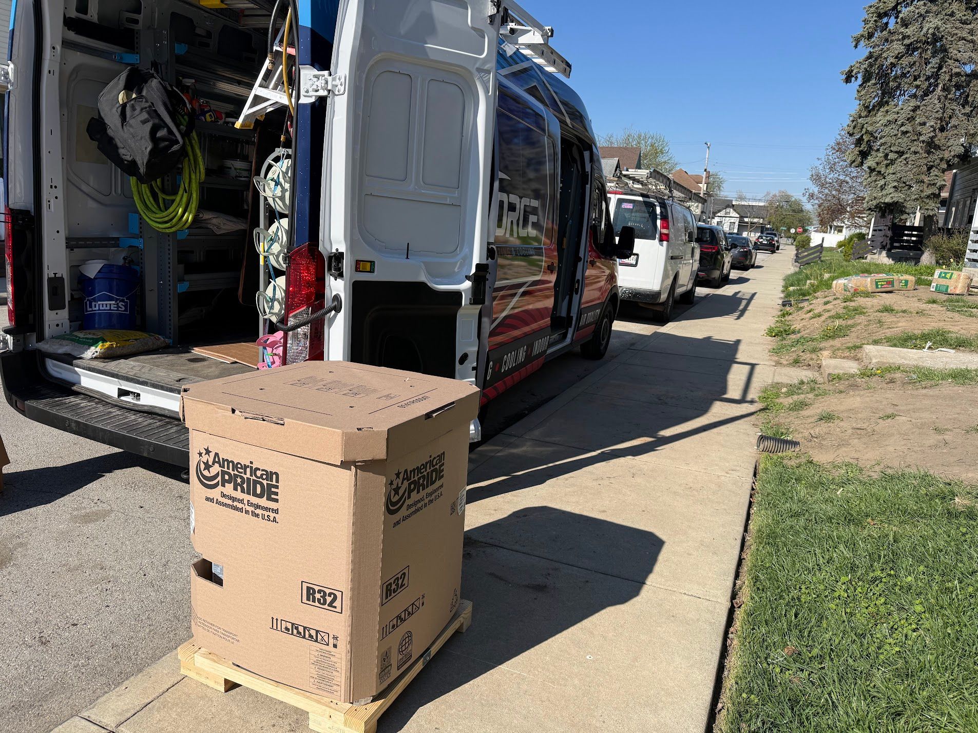 Cardboard boxes beside an open white service van on a sunny residential street