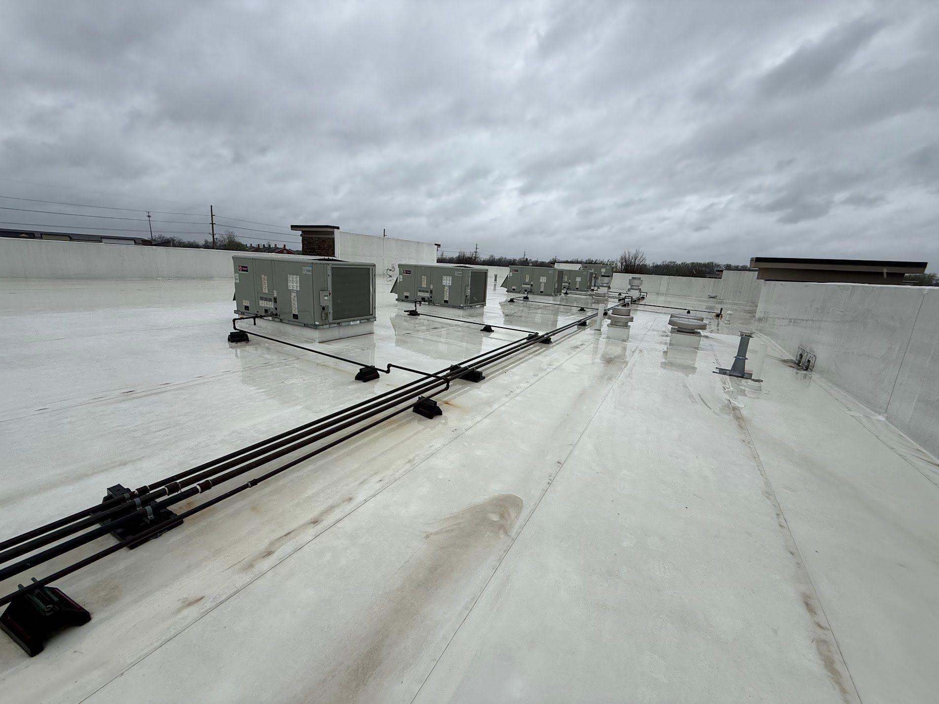 Snow-covered rooftop with HVAC units and black pipes under a cloudy sky
