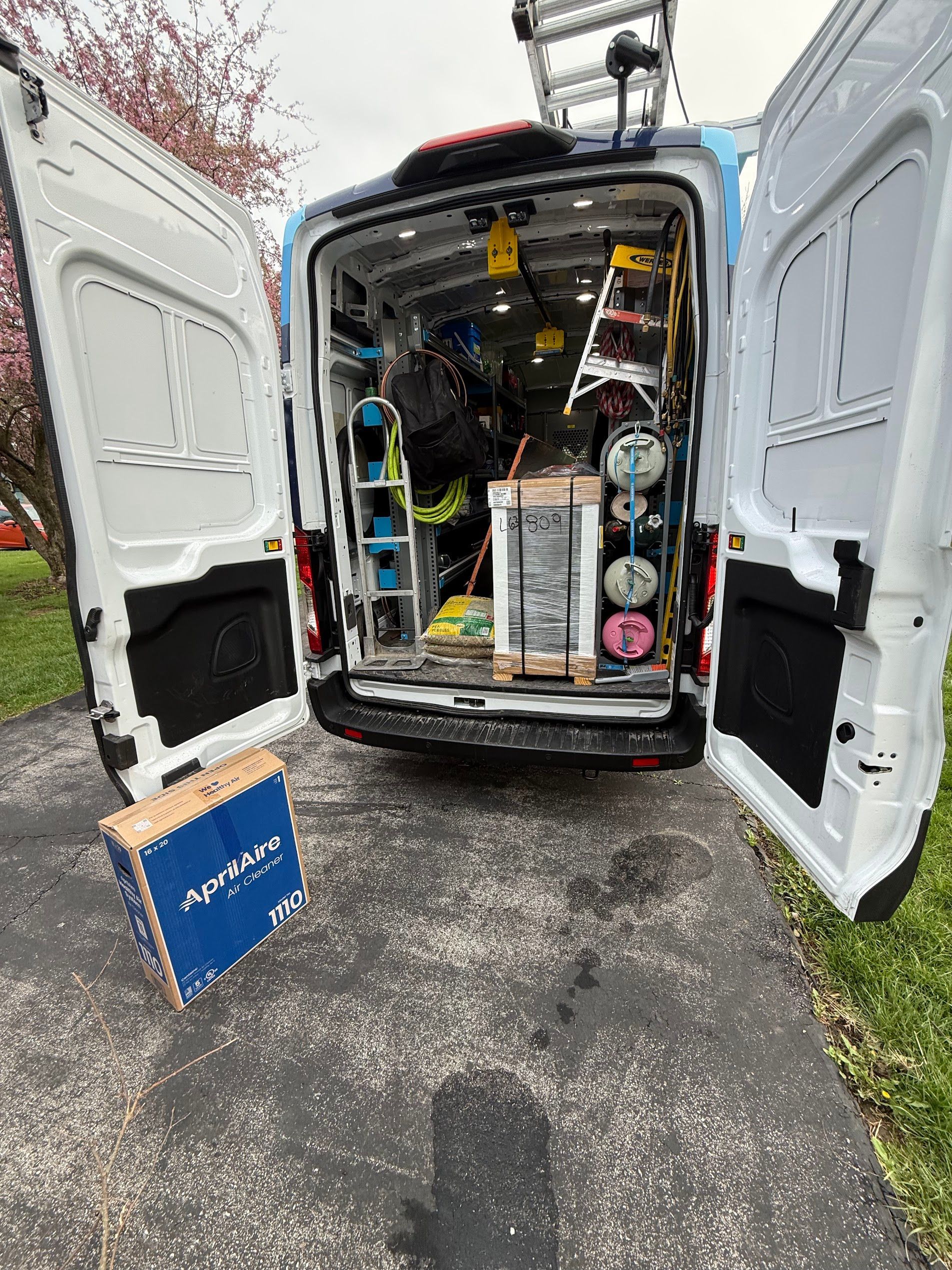 Open van packed with tools and equipment, rear doors open on a driveway.