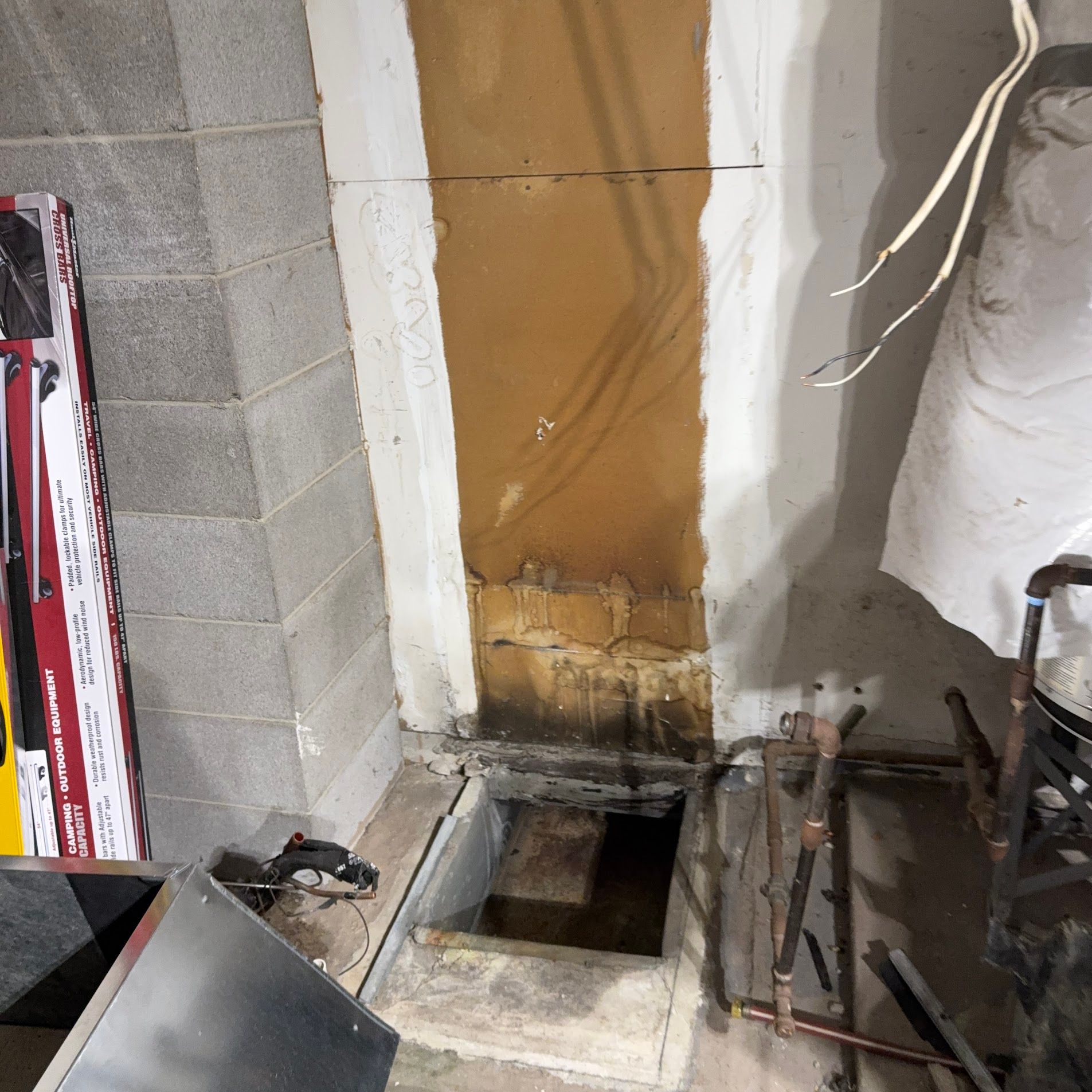 Interior wall opening with exposed framing, pipes, and construction debris in a damaged room