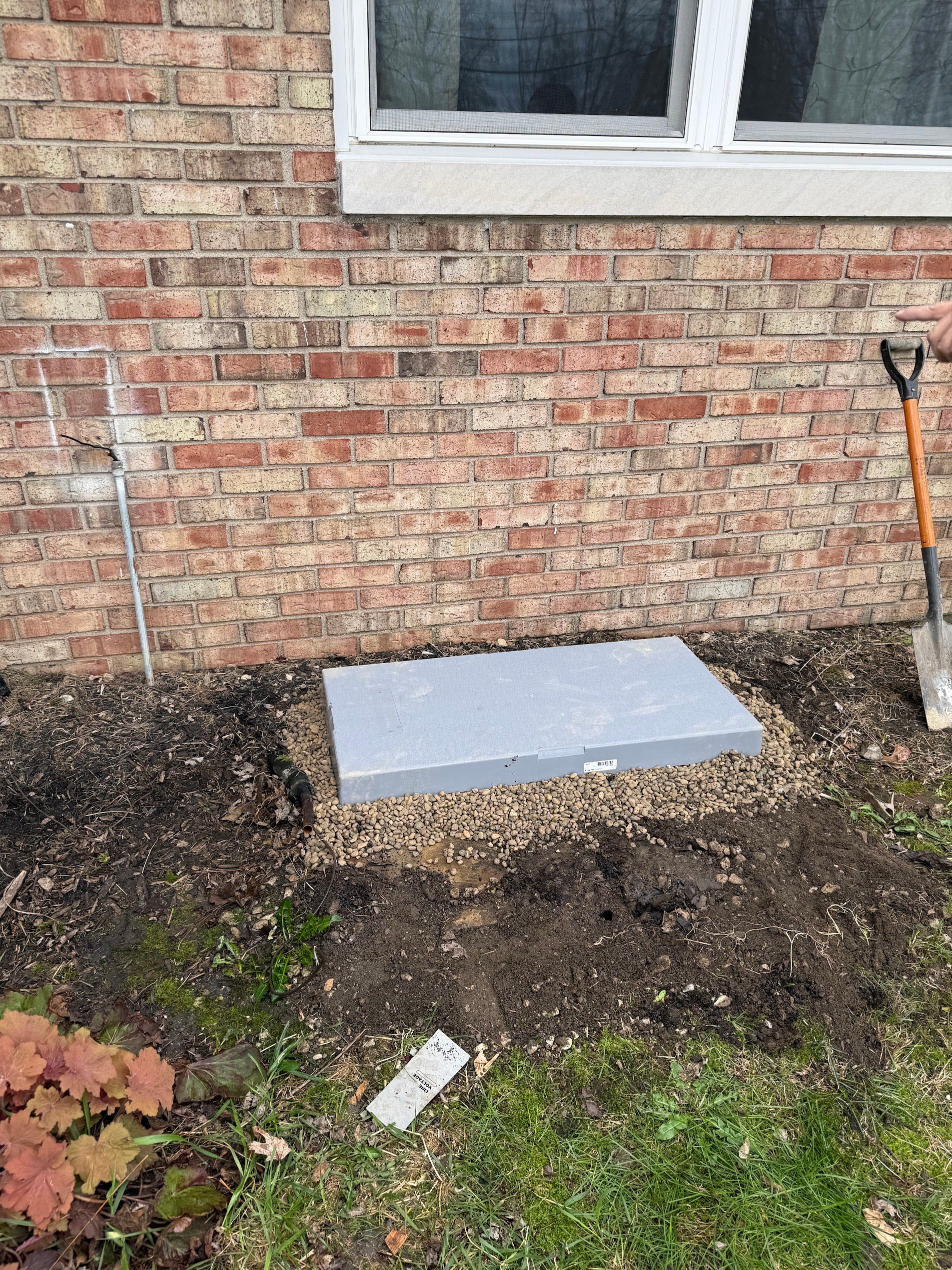 Brick house wall with a small gray concrete slab near a window and garden soil below.
