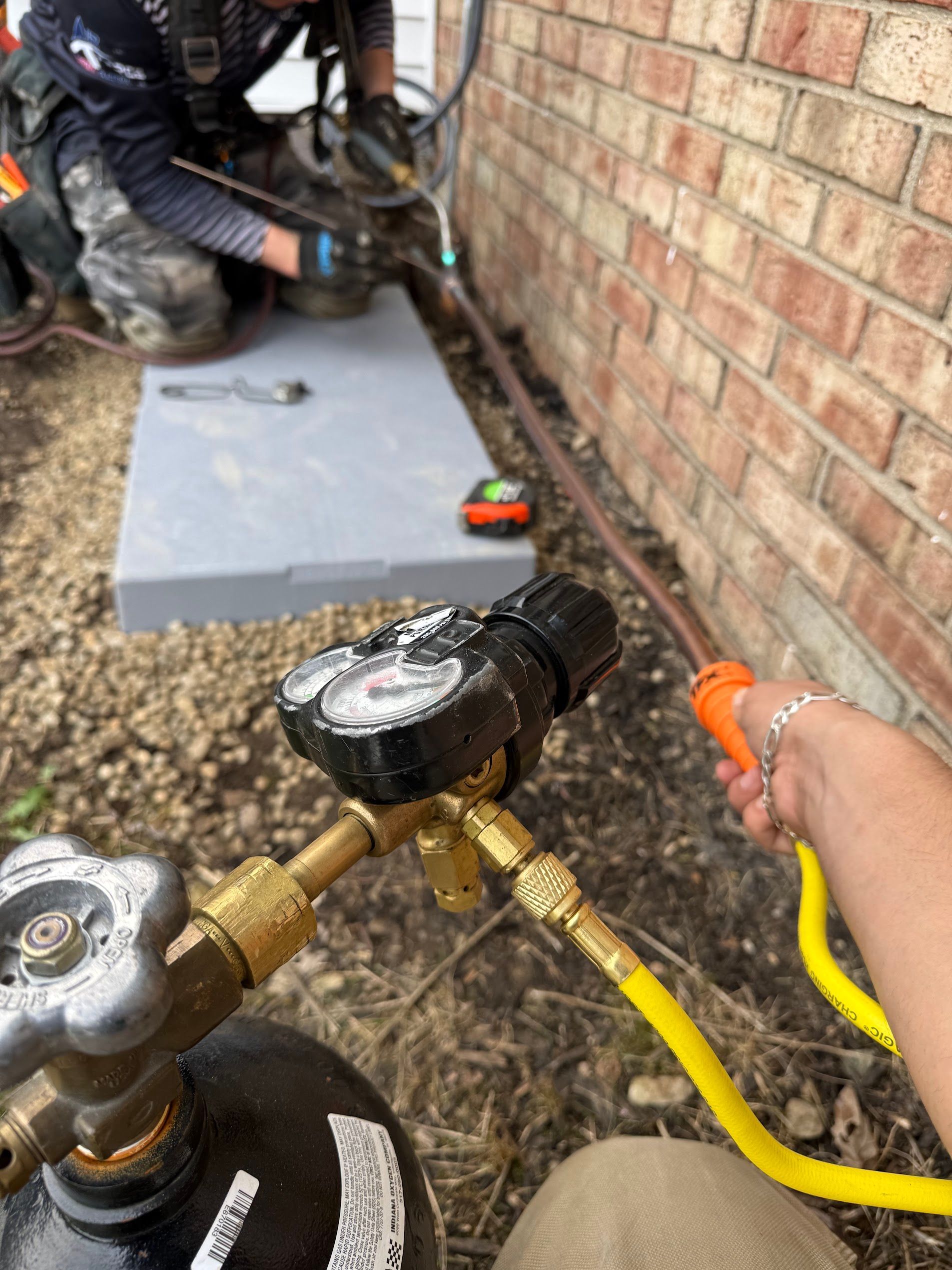 Worker using a hose and gauge near a brick wall and HVAC unit outdoors