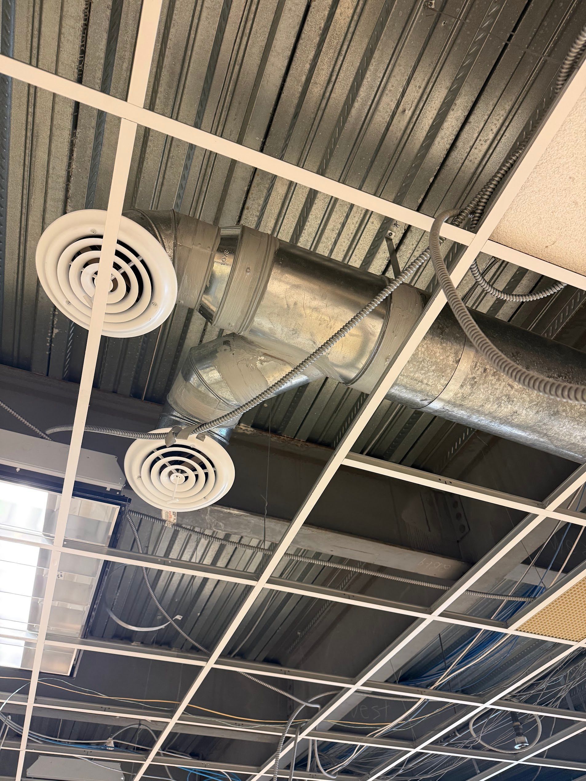 Industrial ceiling with exposed ductwork, circular vents, and a suspended grid ceiling.