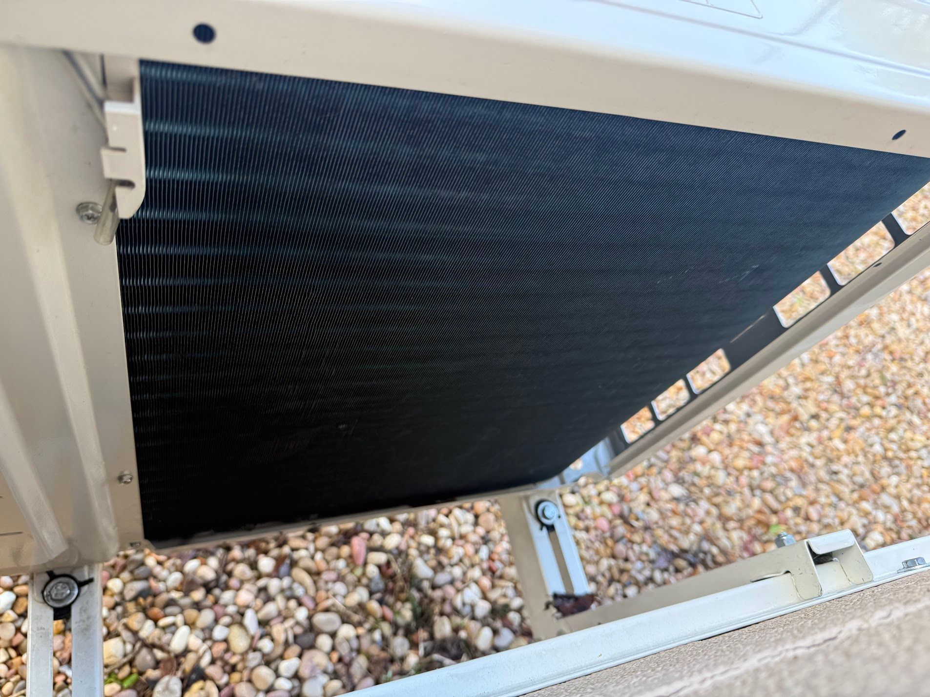 Black mesh privacy screen stretched across a white metal frame over gravel ground