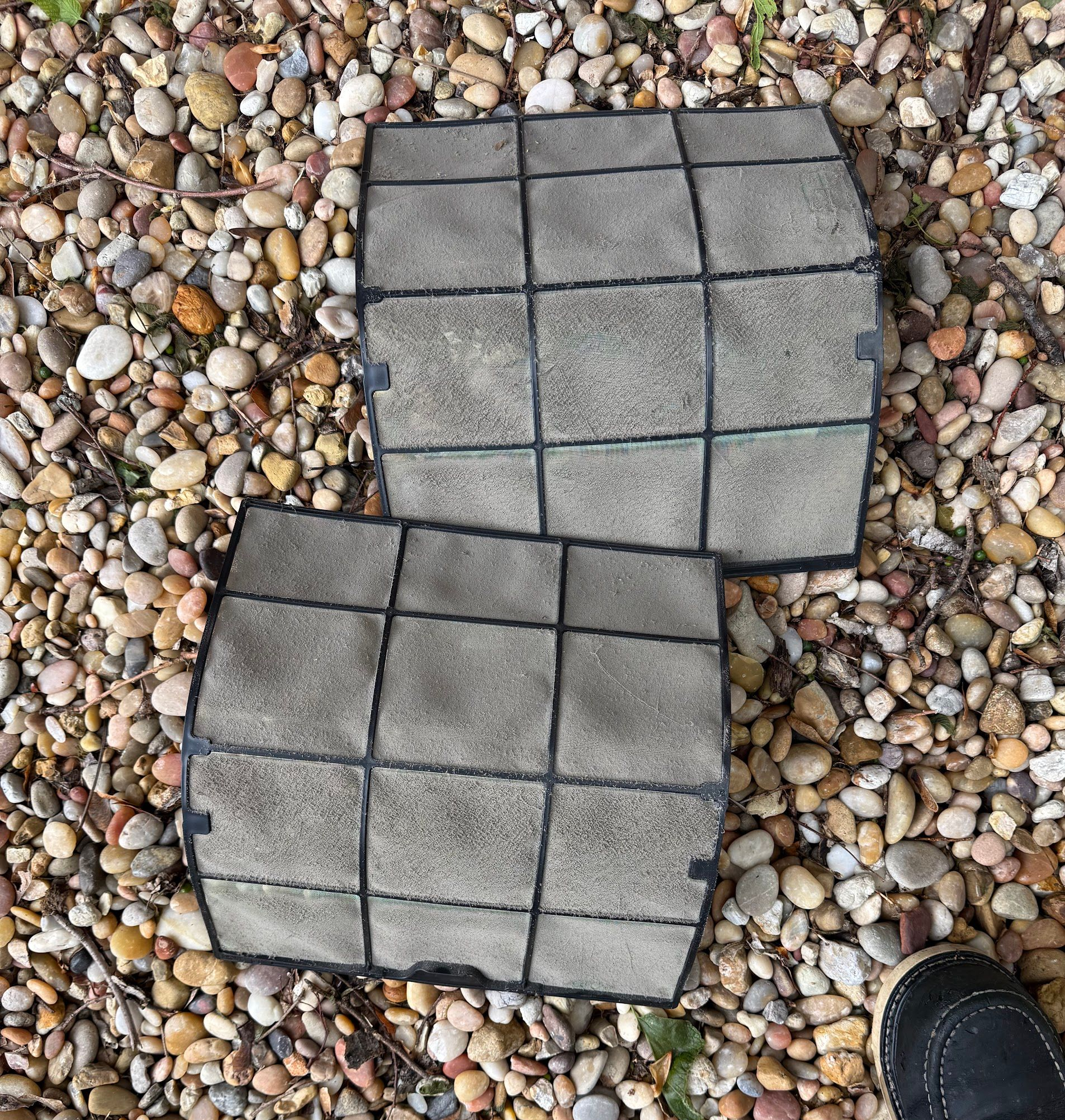 Two gray concrete pavers on pebbled ground, with a black shoe at the lower right.