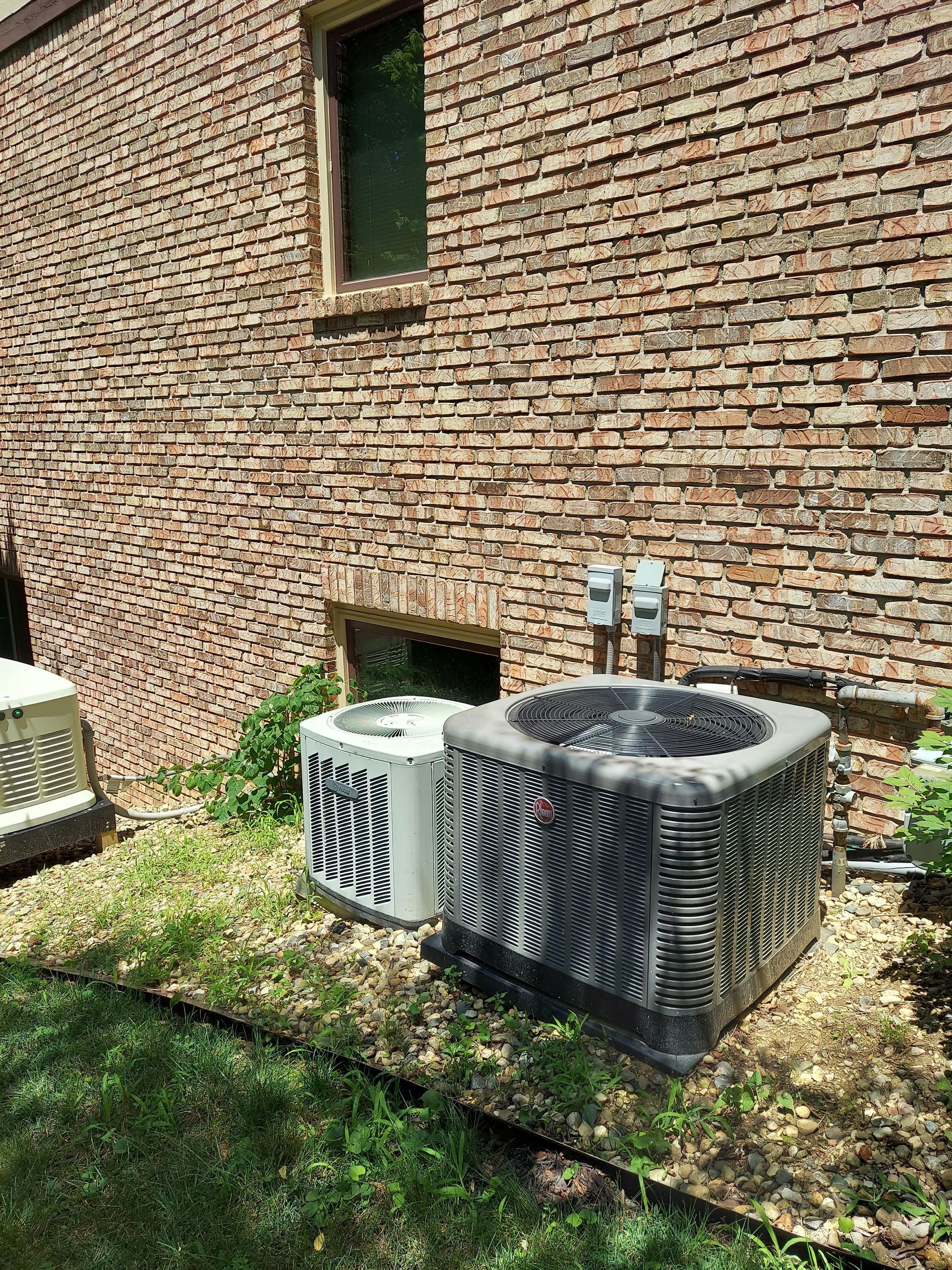 Two air conditioning units near a brick building. One unit is black and gray striped, the other is white and black striped.