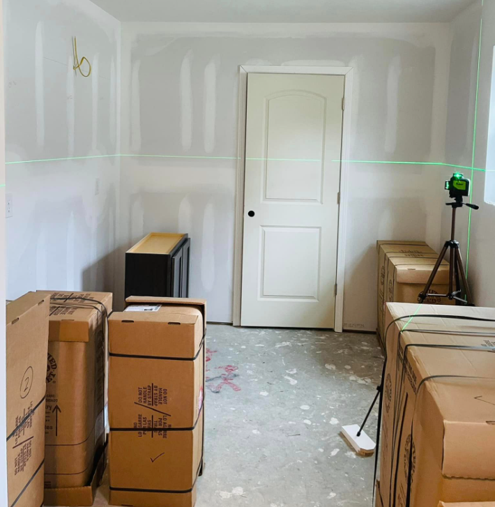 Room under construction with boxes, a door, and a laser level projecting a green line.