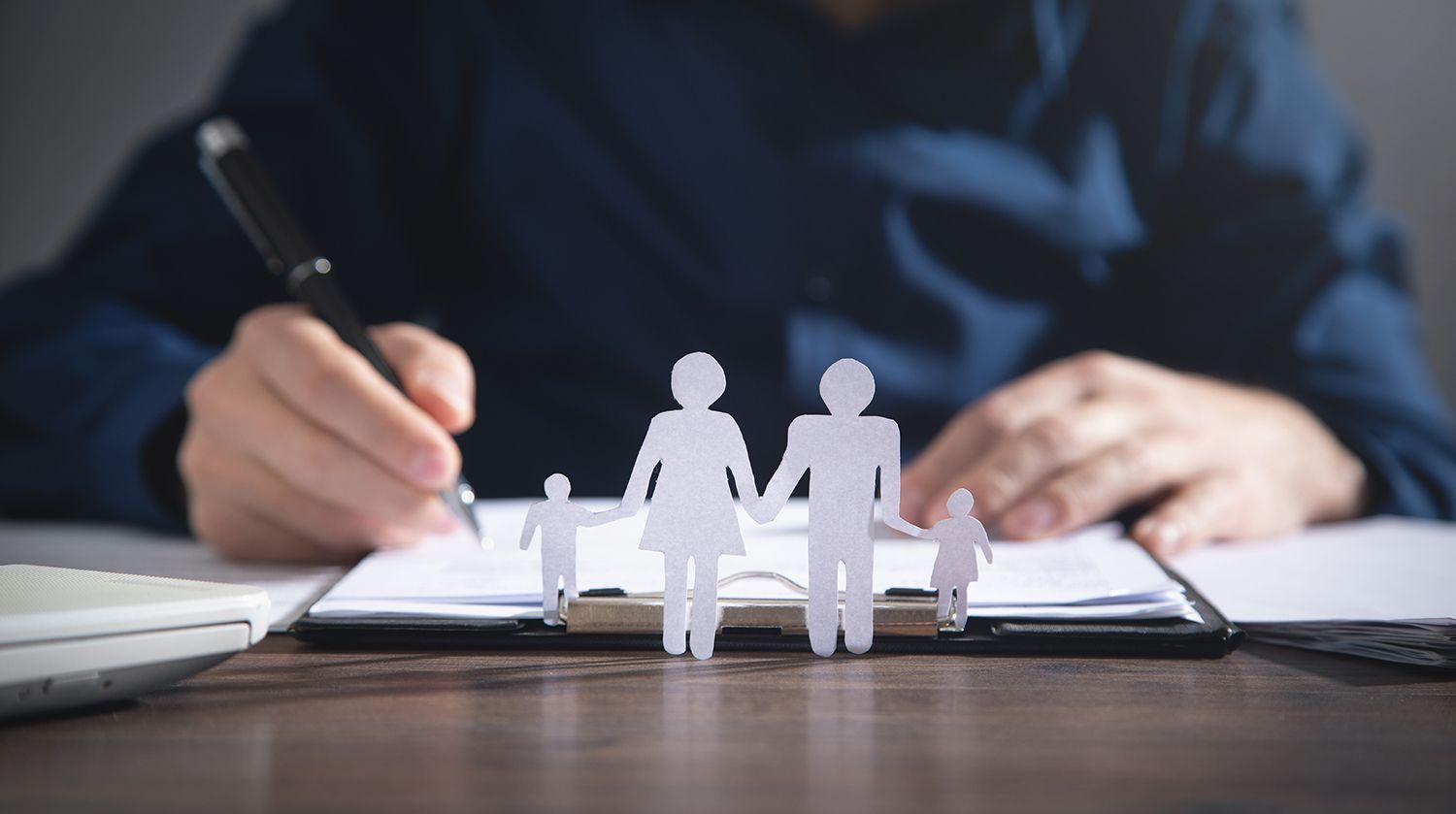 Paper family figures in front of a person signing documents at a desk