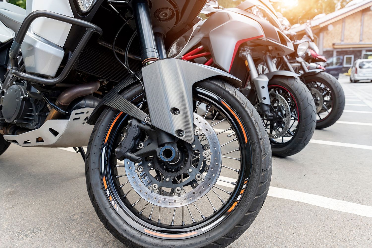 Row of parked motorcycles with close-up front wheel in foreground and warm sunlight behind Row of parked motorcycles with close-up front wheel in foreground and warm sunlight behind