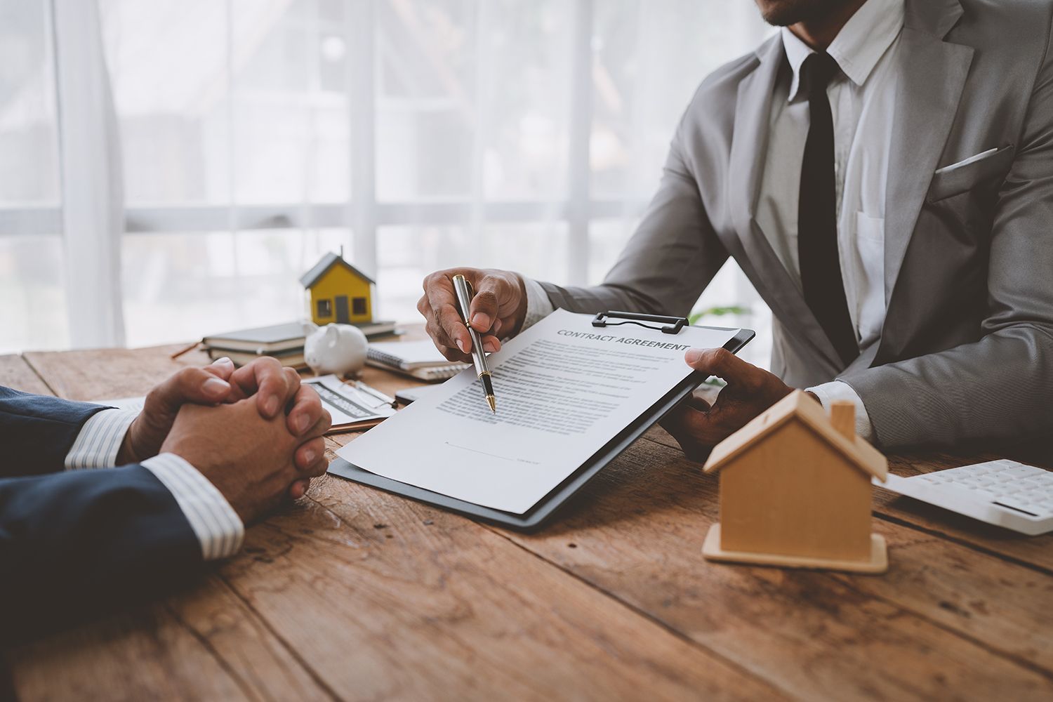 Business meeting with hands reviewing documents and a tablet beside small house models on a wooden table Business meeting with hands reviewing documents and a tablet beside small house models on a wooden table