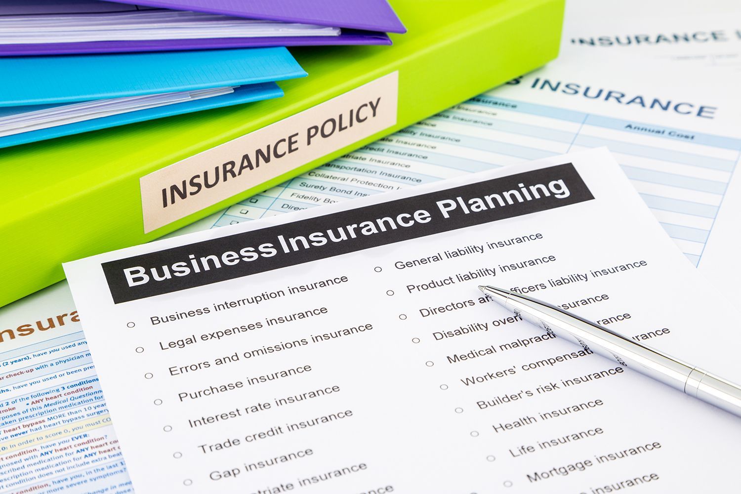 Business insurance planning documents with a pen and stacked folders on a desk Business insurance planning documents with a pen and stacked folders on a desk