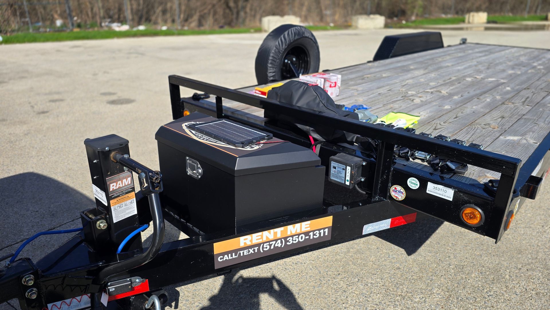 Utility trailer with black toolboxes and a spare tire parked on pavement outdoors