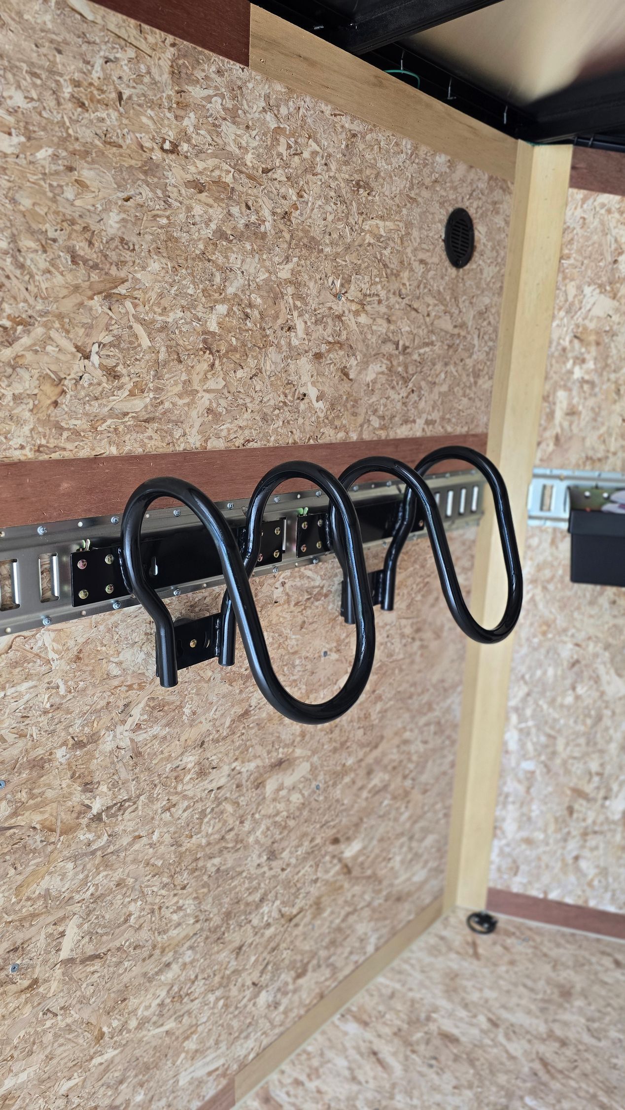 Black coiled cables hanging on a metal rail inside a plywood-lined storage area