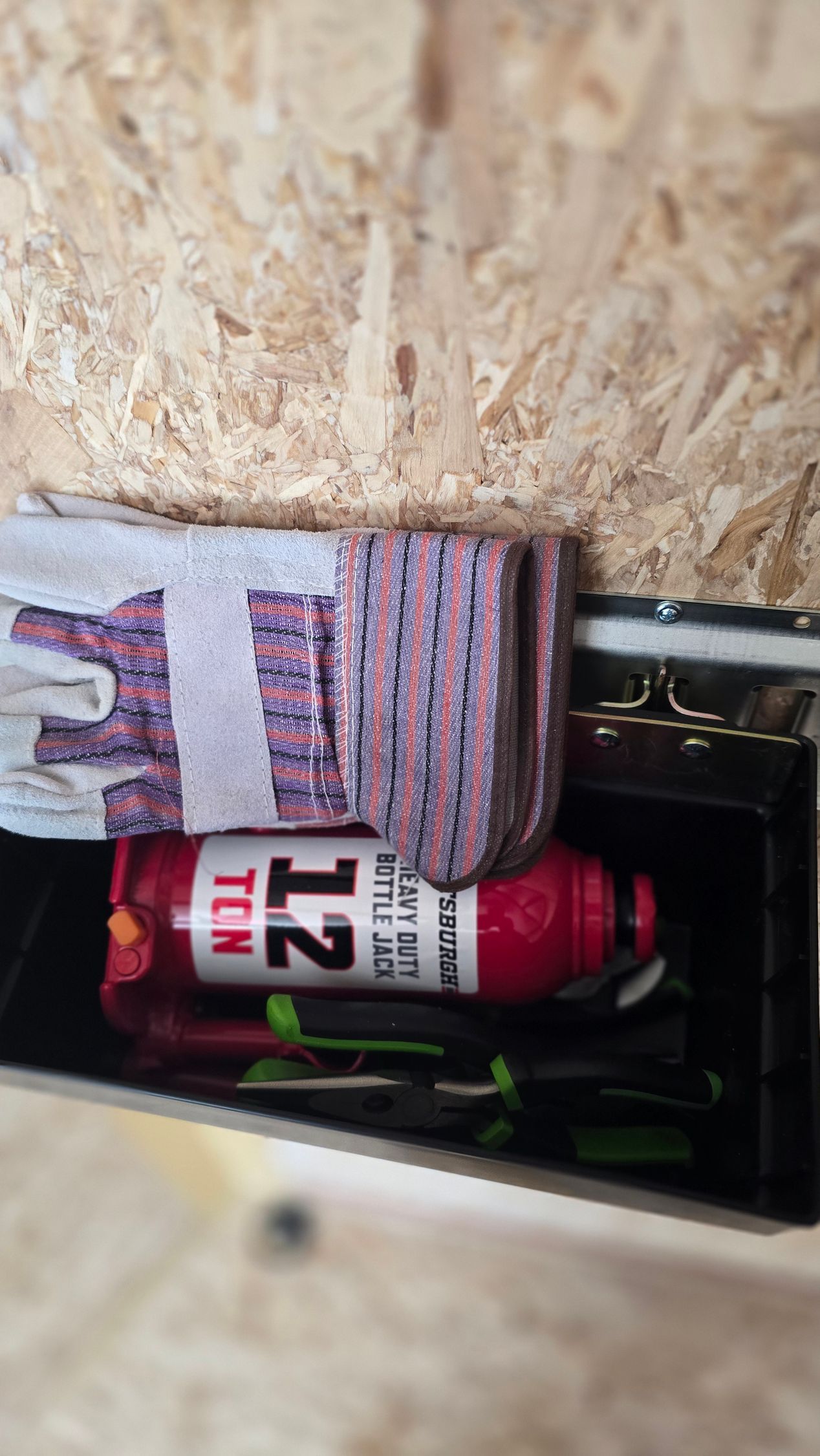 Hand holding a red can beside a striped glove and a wooden wall opening