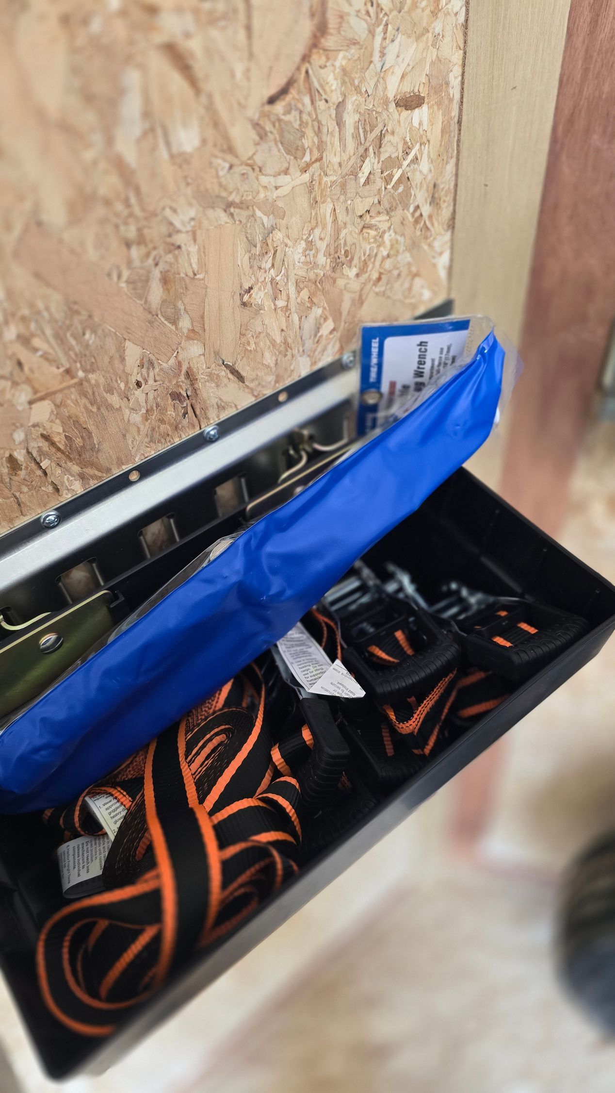 Open toolbox with orange-and-black cords and tools beside a wood-paneled wall