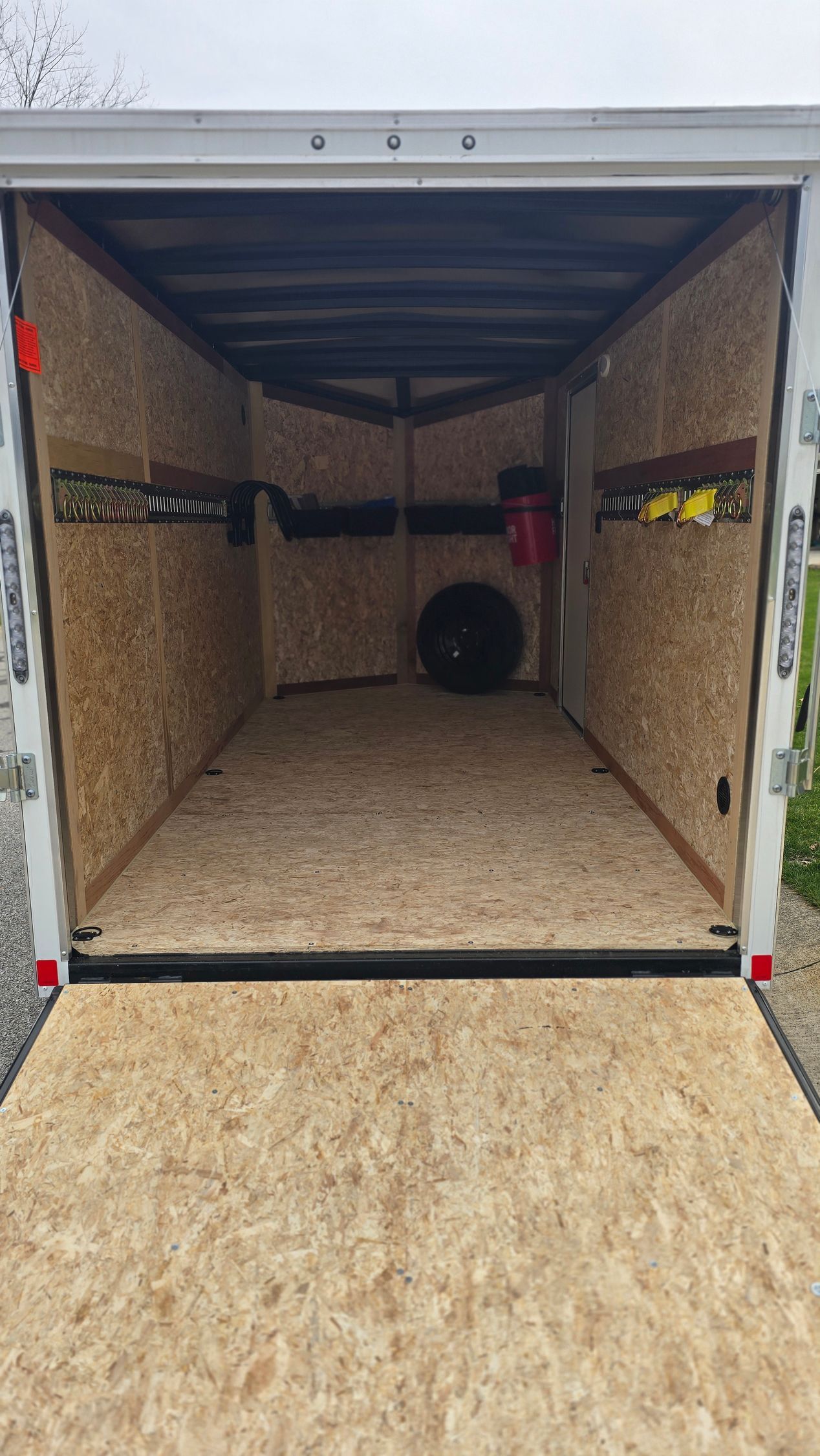 Open cargo trailer interior with plywood walls and floor, viewed from the open rear door.