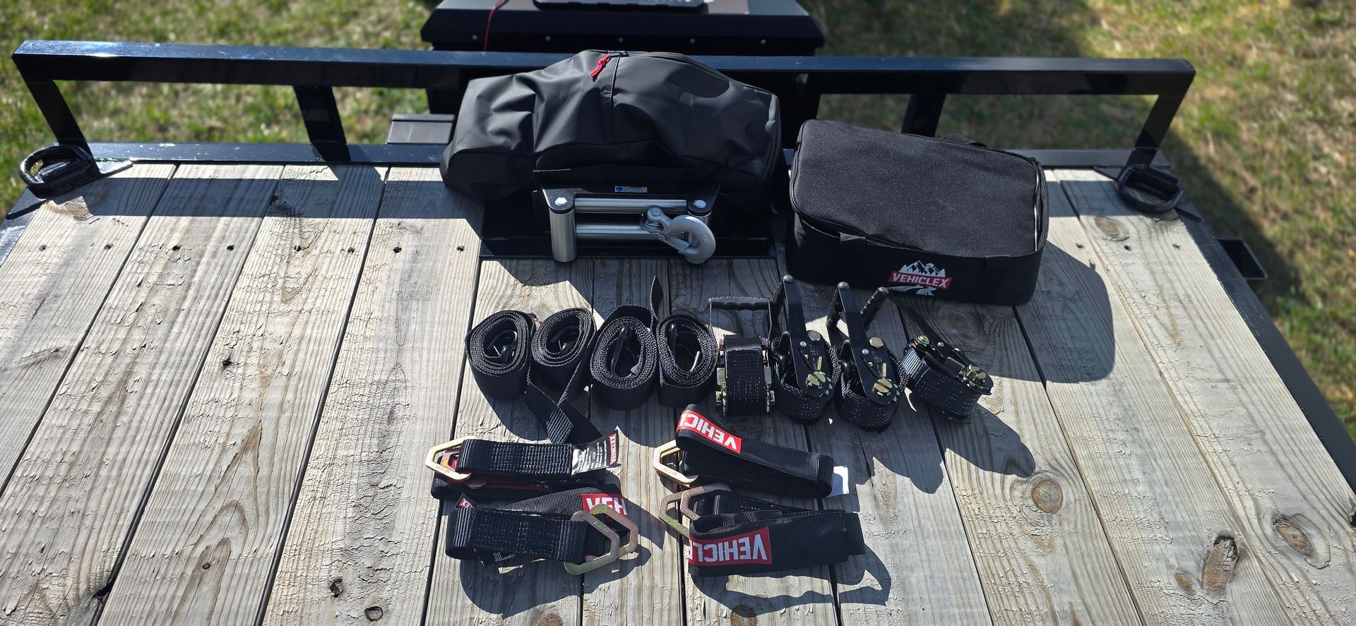Camera gear and bags laid out on a wooden dock beside a black bench in bright sunlight