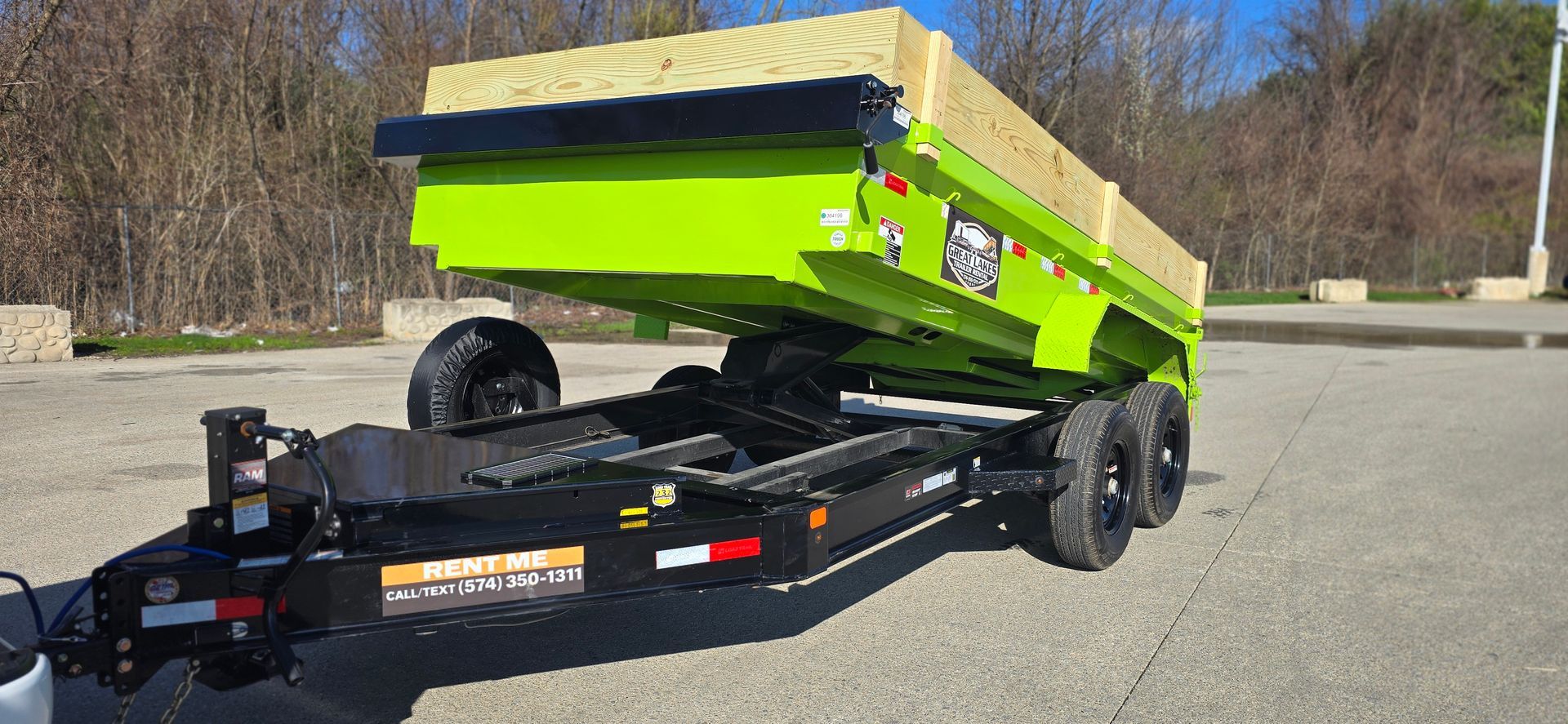 Bright green dump trailer tilted in an outdoor parking lot, with wooden boards on top in Bristol Indiana.