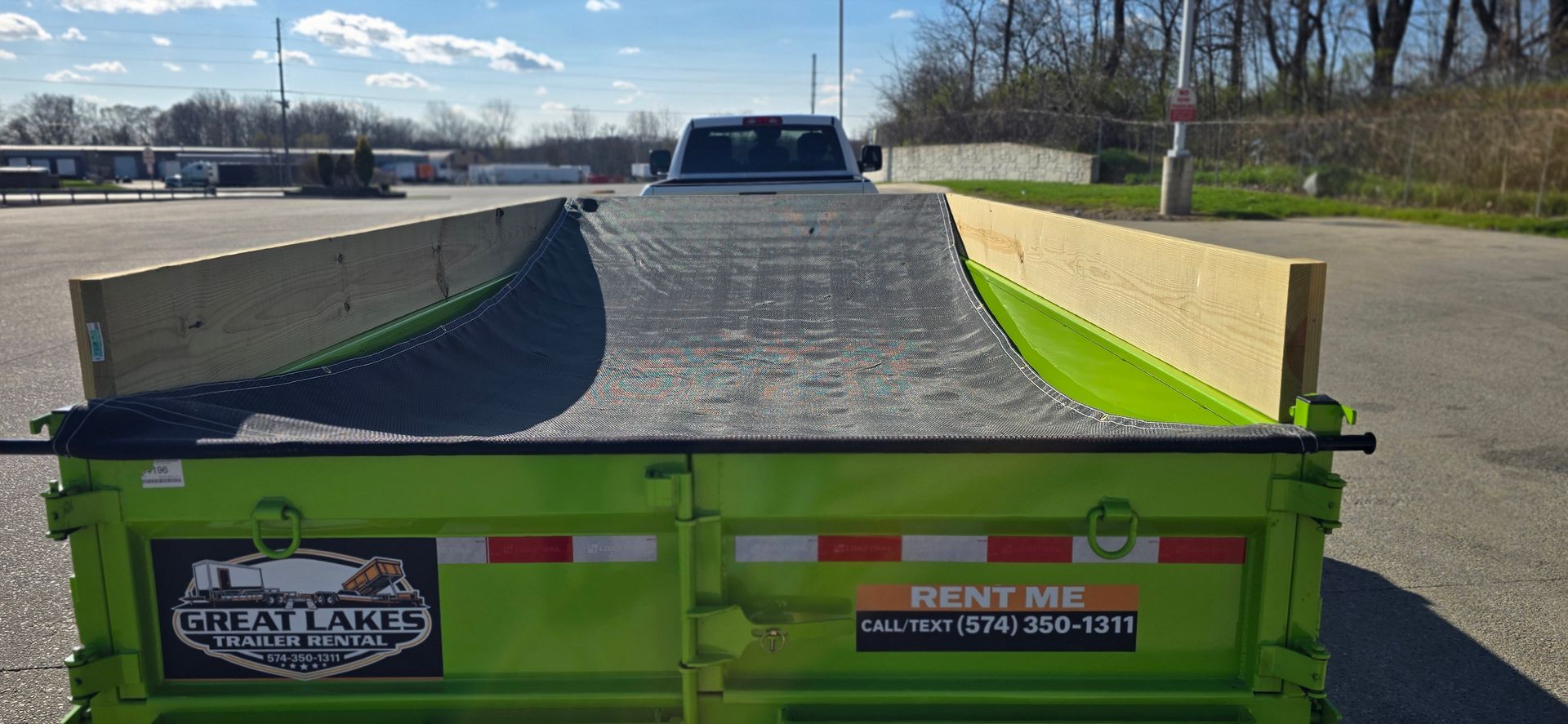 Green dump trailer loaded with crushed stone on a road under a sunny sky