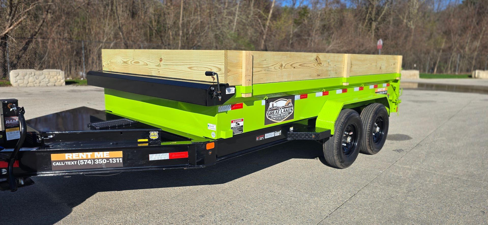 Bright green utility trailer loaded with boxes, parked on a gravel lot near woods.