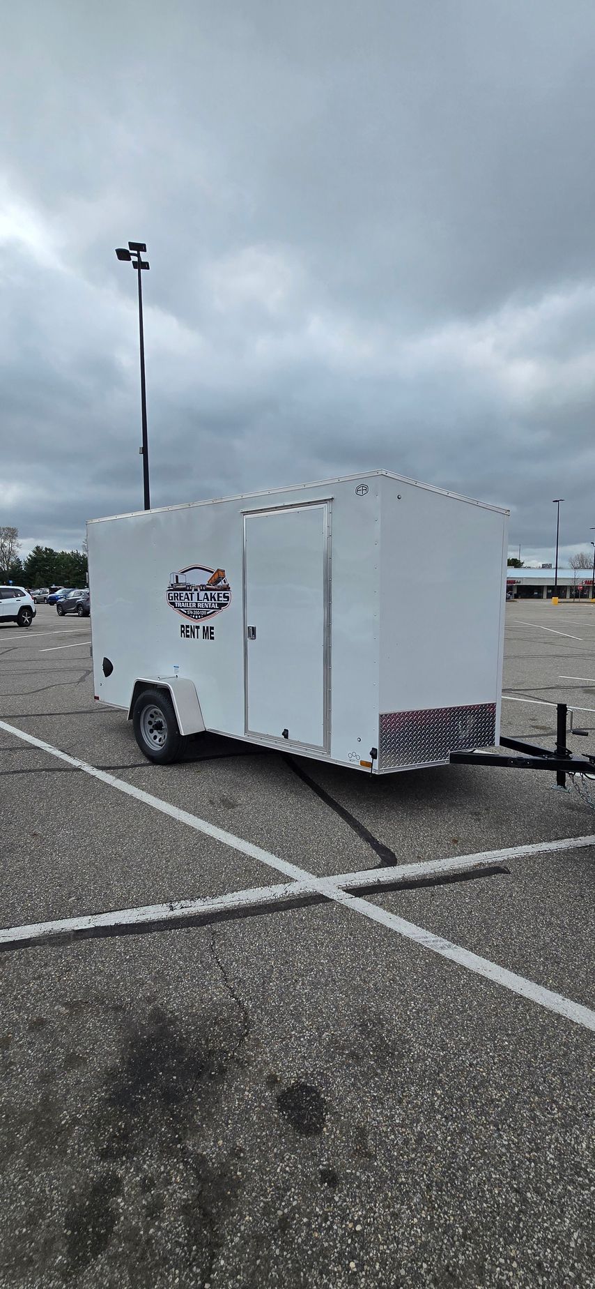 White enclosed utility trailer parked in an empty lot under a cloudy sky in Goshen Indiana.