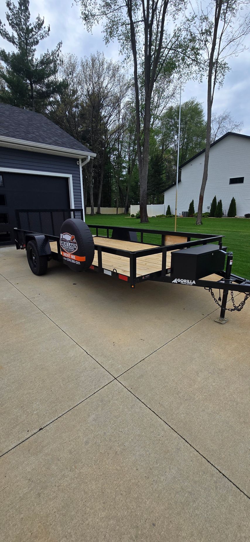 Utility trailer parked in a driveway beside a garage, with a lawn and houses in the background in Elkhart Indiana.