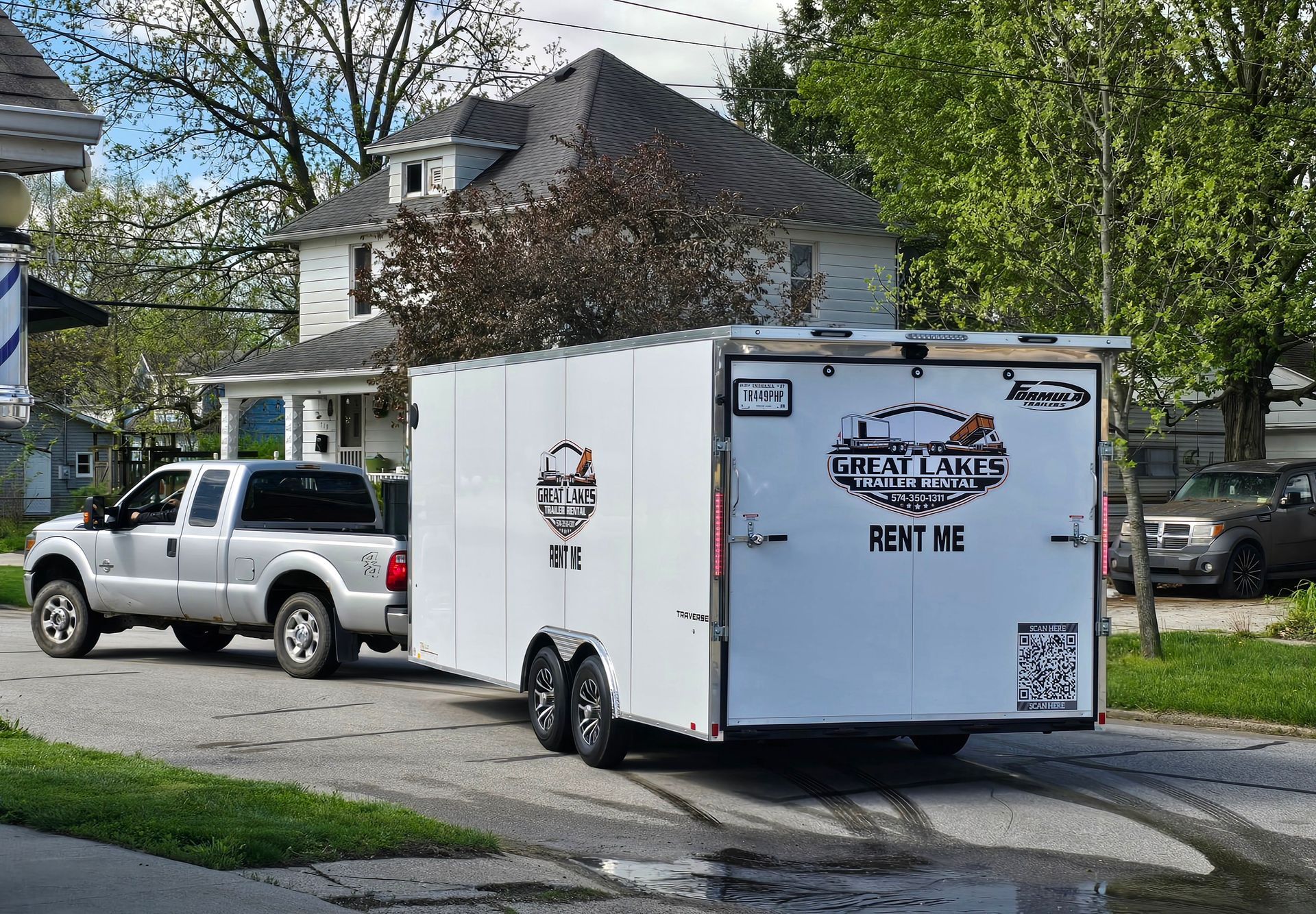 White enclosed trailer with business logo parked behind a silver pickup on a suburban street.