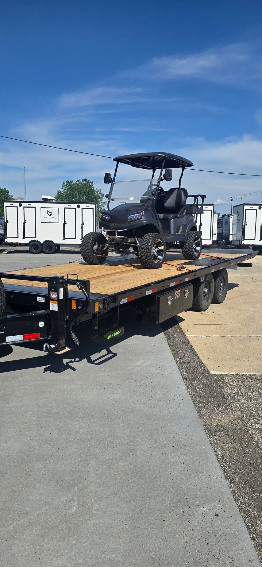 Black golf cart on a flatbed trailer in a yard under a blue sky