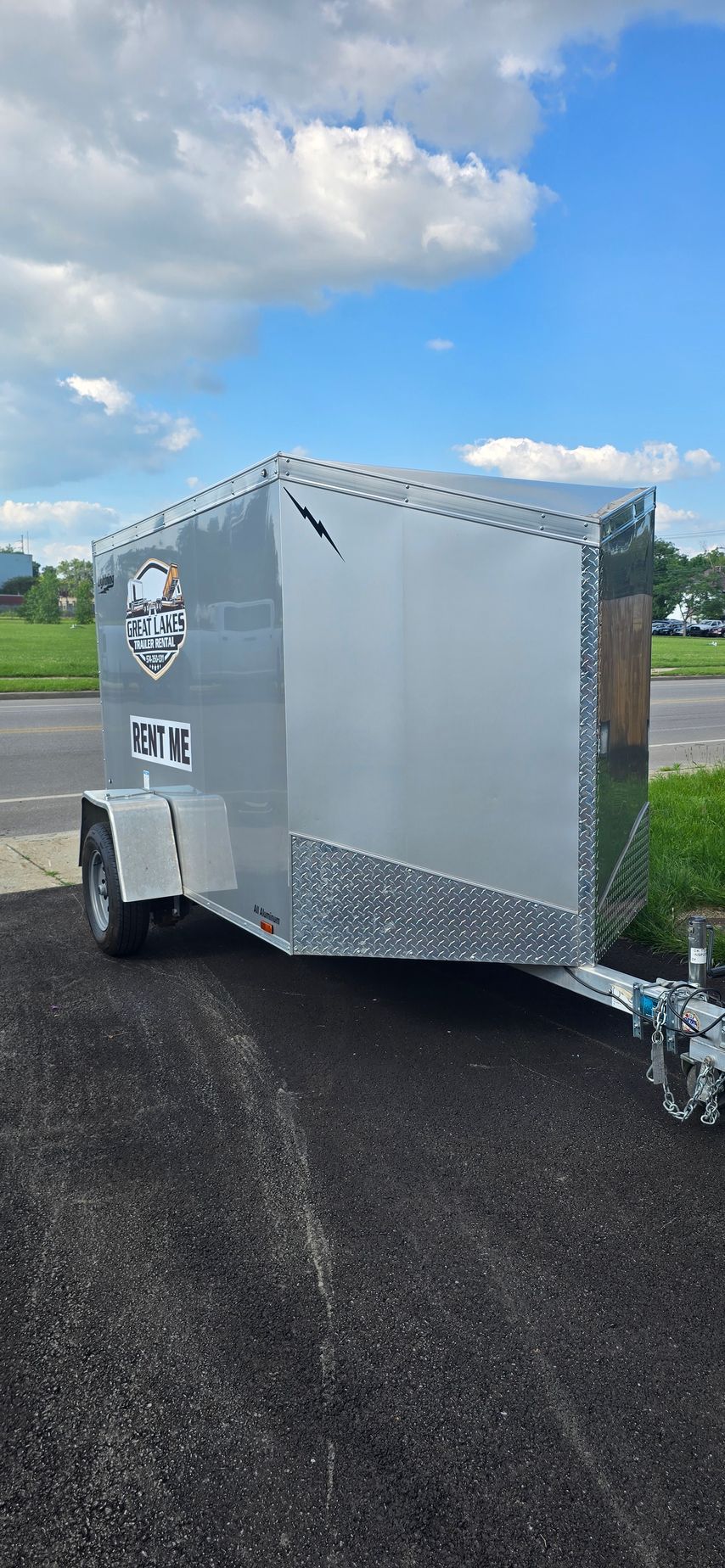 Silver enclosed trailer parked on a roadside under a partly cloudy sky