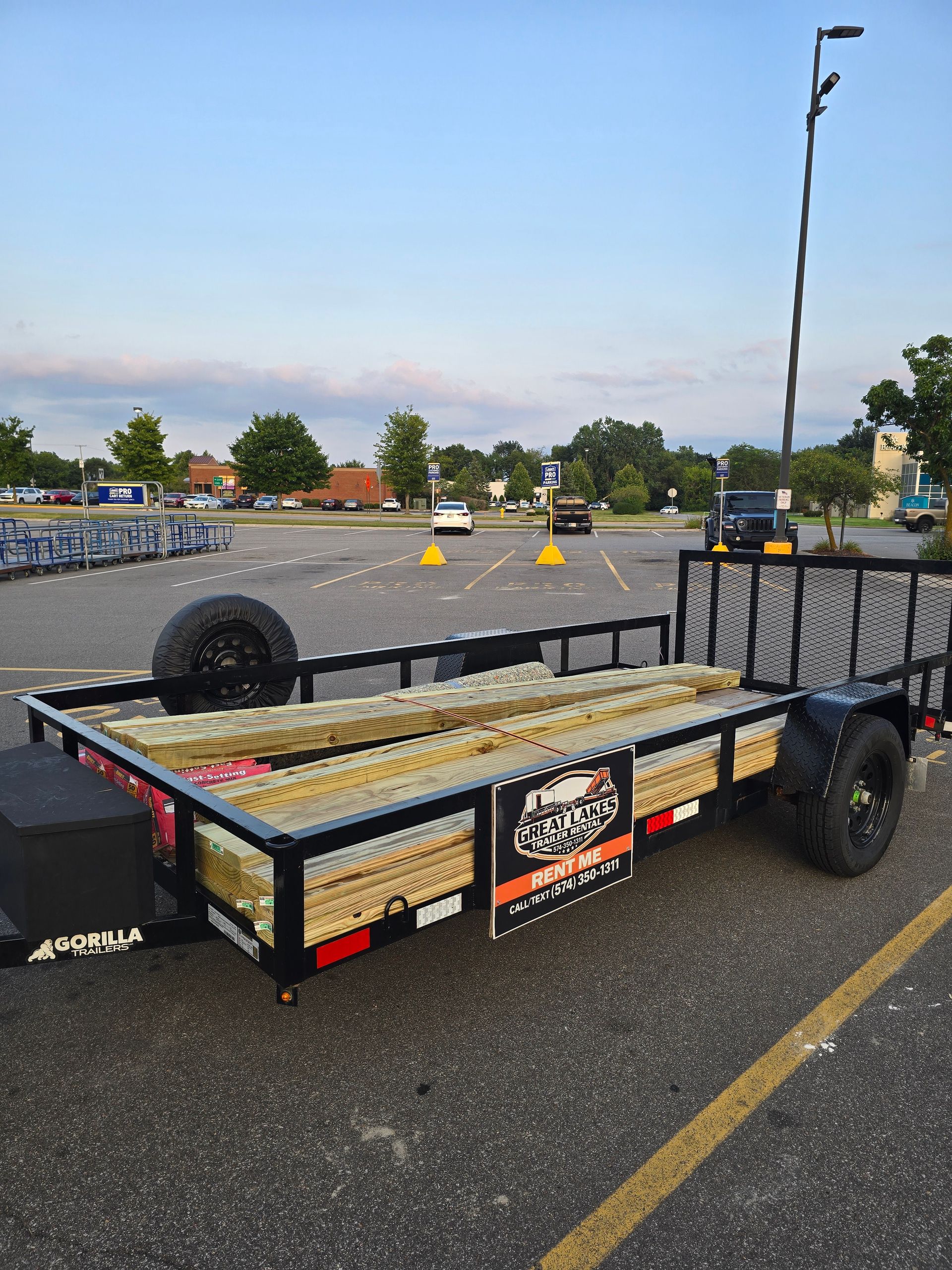 Small flatbed utility trailer parked in a lot, loaded with materials and marked with decals.