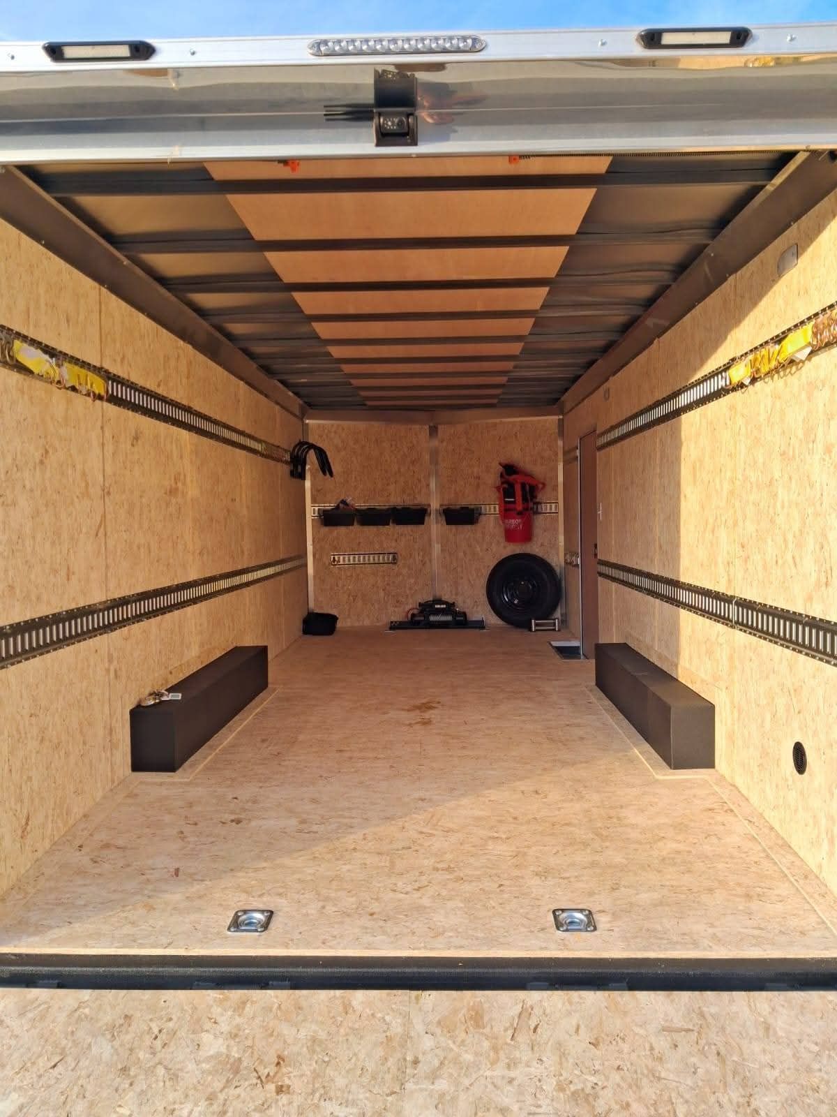 Open cargo trailer with plywood floor and walls, empty inside except for a few tools and items at the back.