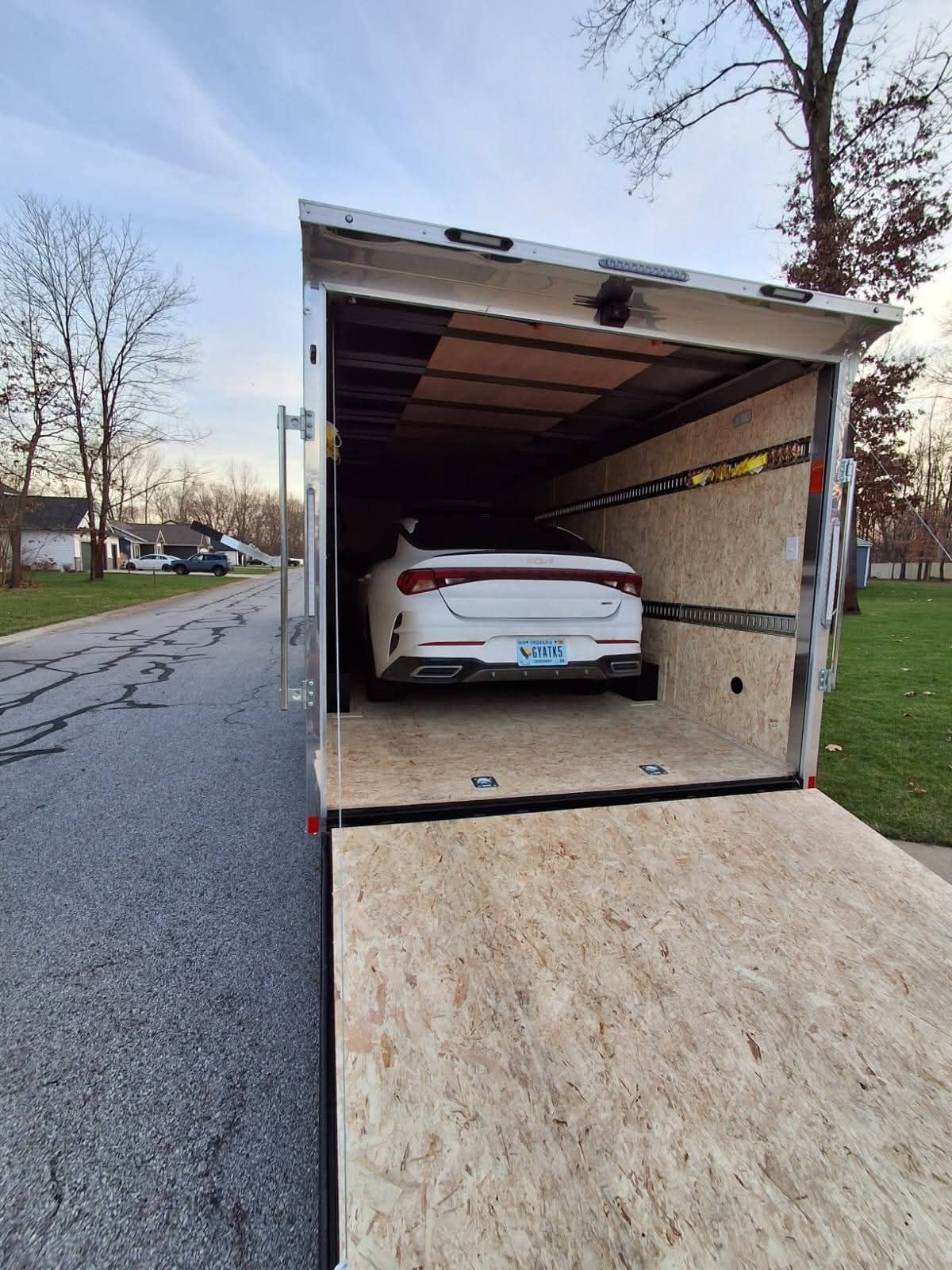 White car secured inside a small open trailer on a roadside.
