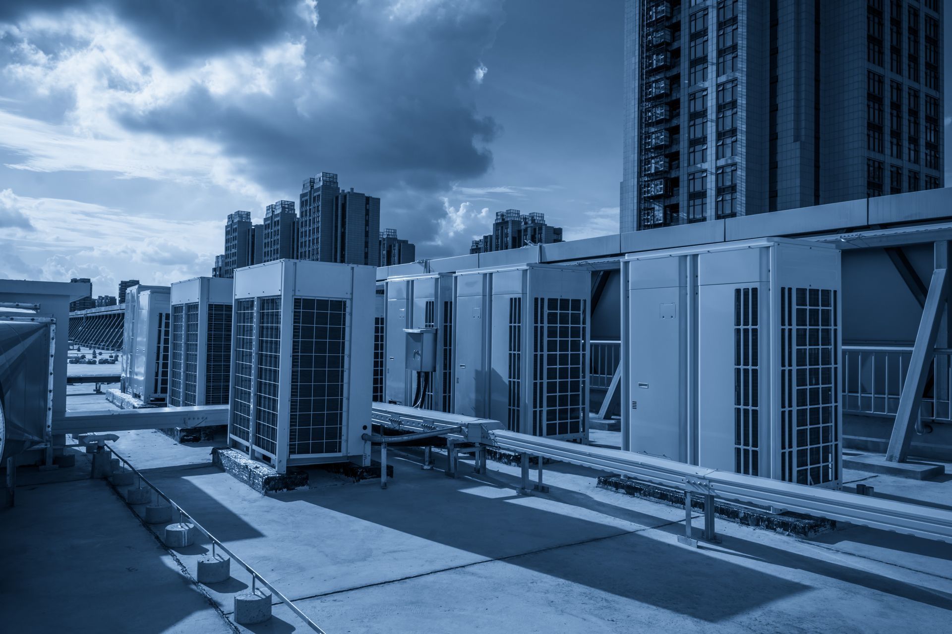 Rooftop with HVAC units and railings under a cloudy sky beside tall buildings